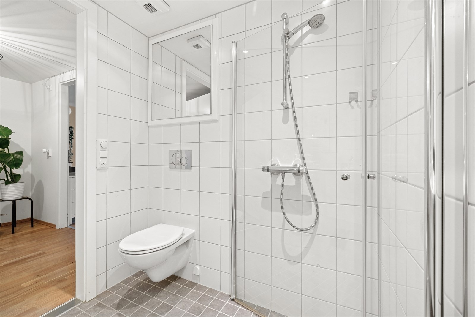 Badet har dusj med innfellbare dusjdører. Vegghengt toalett og veggspeil som skjuler rørskapet. Galleribilde