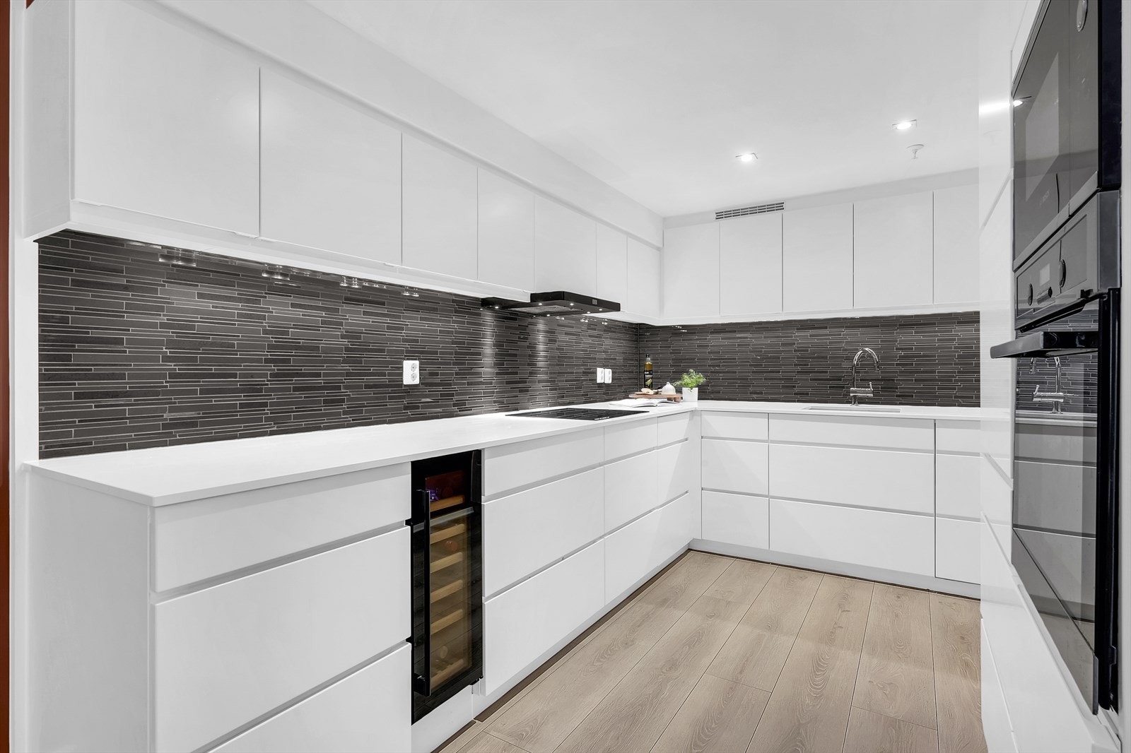 Stilig innredning med hvite, glatte fronter og benkeplate i stein med nedfelt vask. Galleribilde