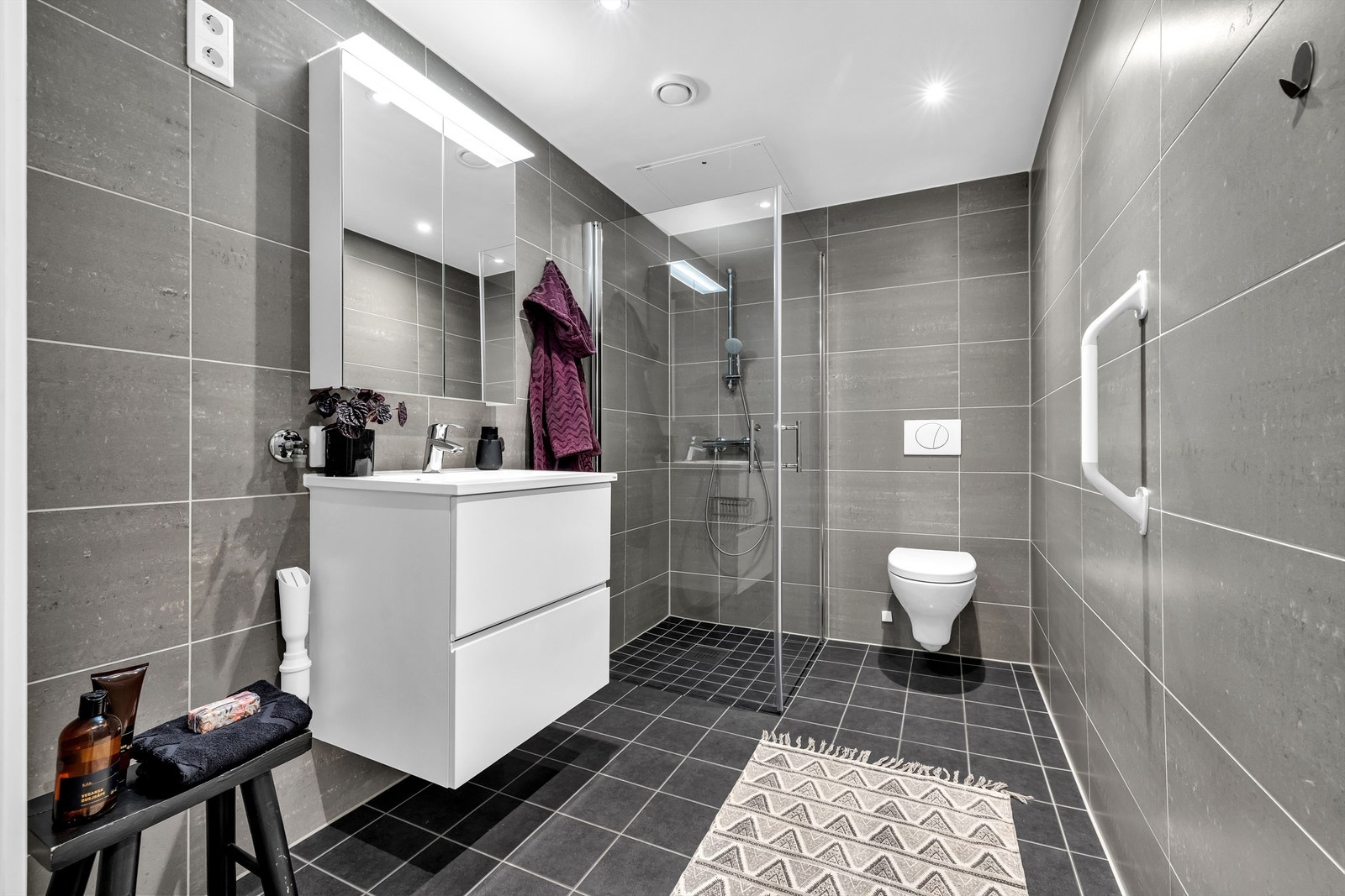 Lekkert bad med mørke fliser på gulv og vegger. Opplegg for vaskemaskin og tørketrommel. Galleribilde