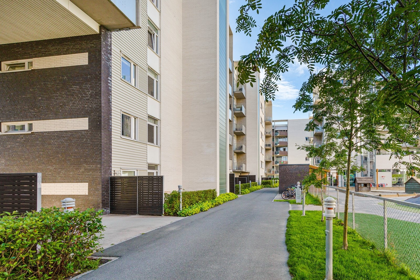 Fellesarealer opparbeidet med asfalterte adkomstveier, gressplen, trær, diverse beplantning, sittegrupper og lekeplasser. Galleribilde