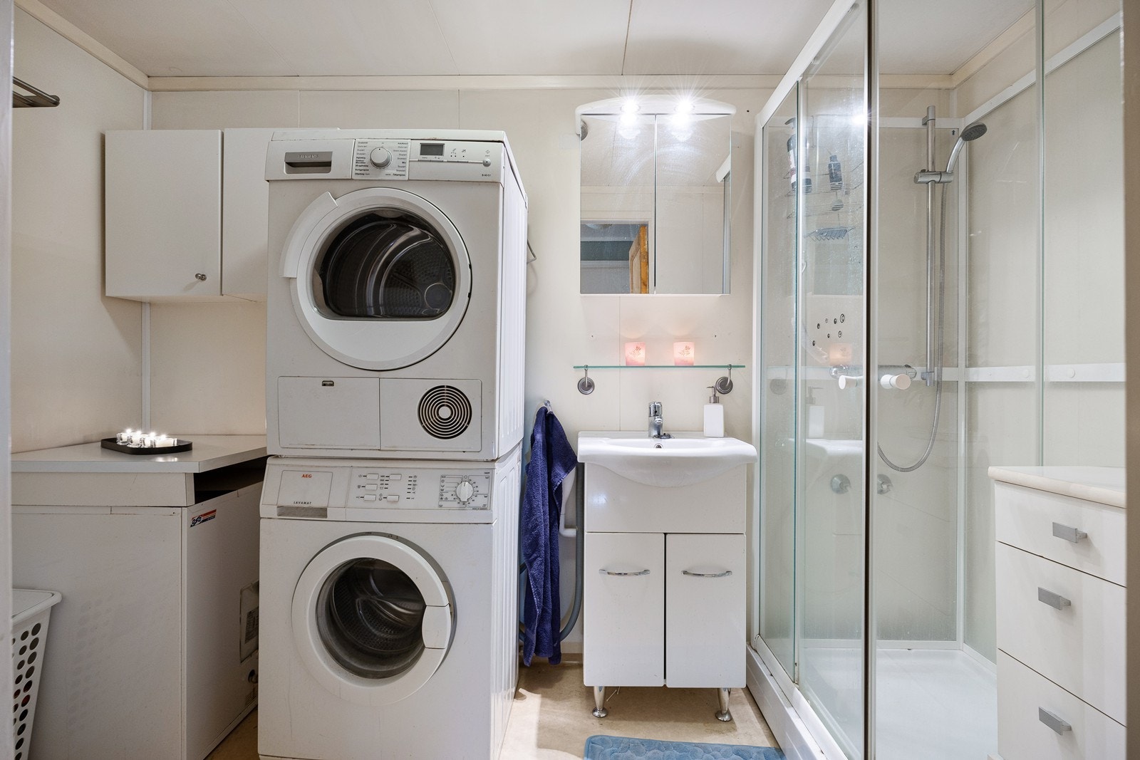 Baderom innredet med servant i servantskap, speilskap, dusjkabinett, toalett og opplegg for vaskemaskin og tørketrommel. Galleribilde