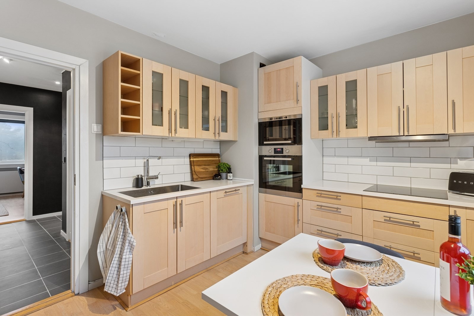 Kjøkkeninnredning har profilerte, heltre fronter, 6 overskap med glass, laminat benkeplate, kullfilterventilator, underlimt og nedfelt stål benkebeslag. Galleribilde