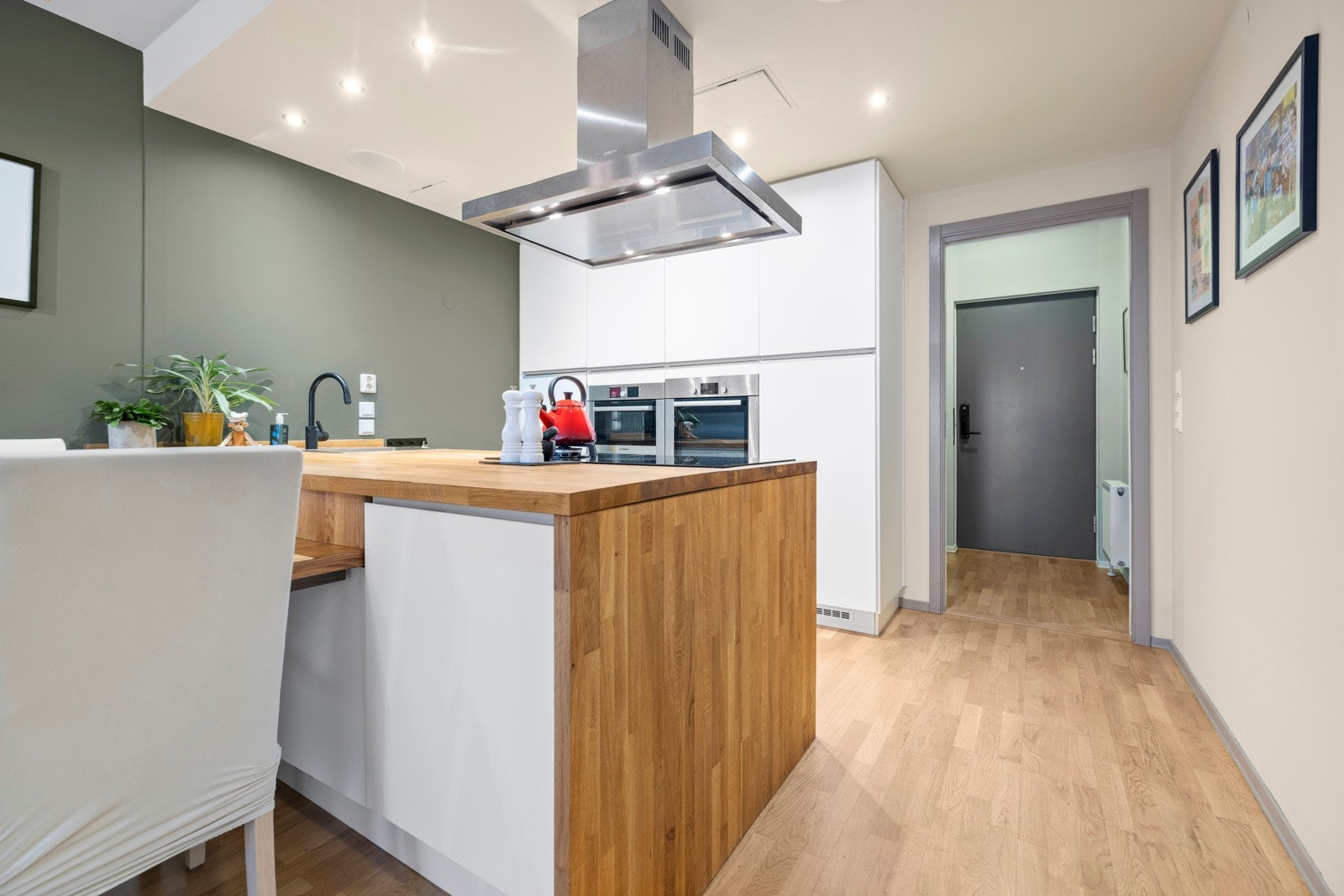 Moderne og stilrent kjøkken i åpen løsning mot stuen med god skap- og benkeplass. Hvite, glatte fronter på skapdører og skuffer, og benkeplate i heltre med nedfelt kum Galleribilde