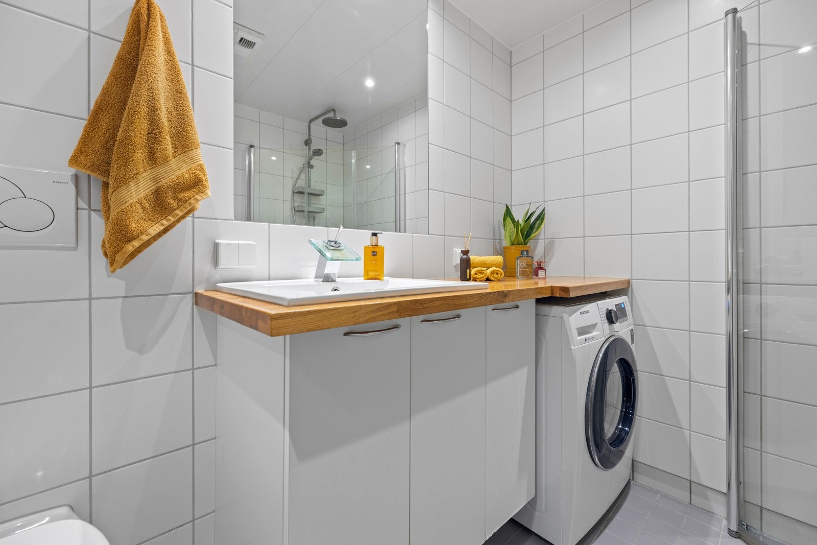 Baderommet har servantskap med overliggende servant med oppbevaringsplass og stort speil over, og opplegg for vaskemaskin Galleribilde