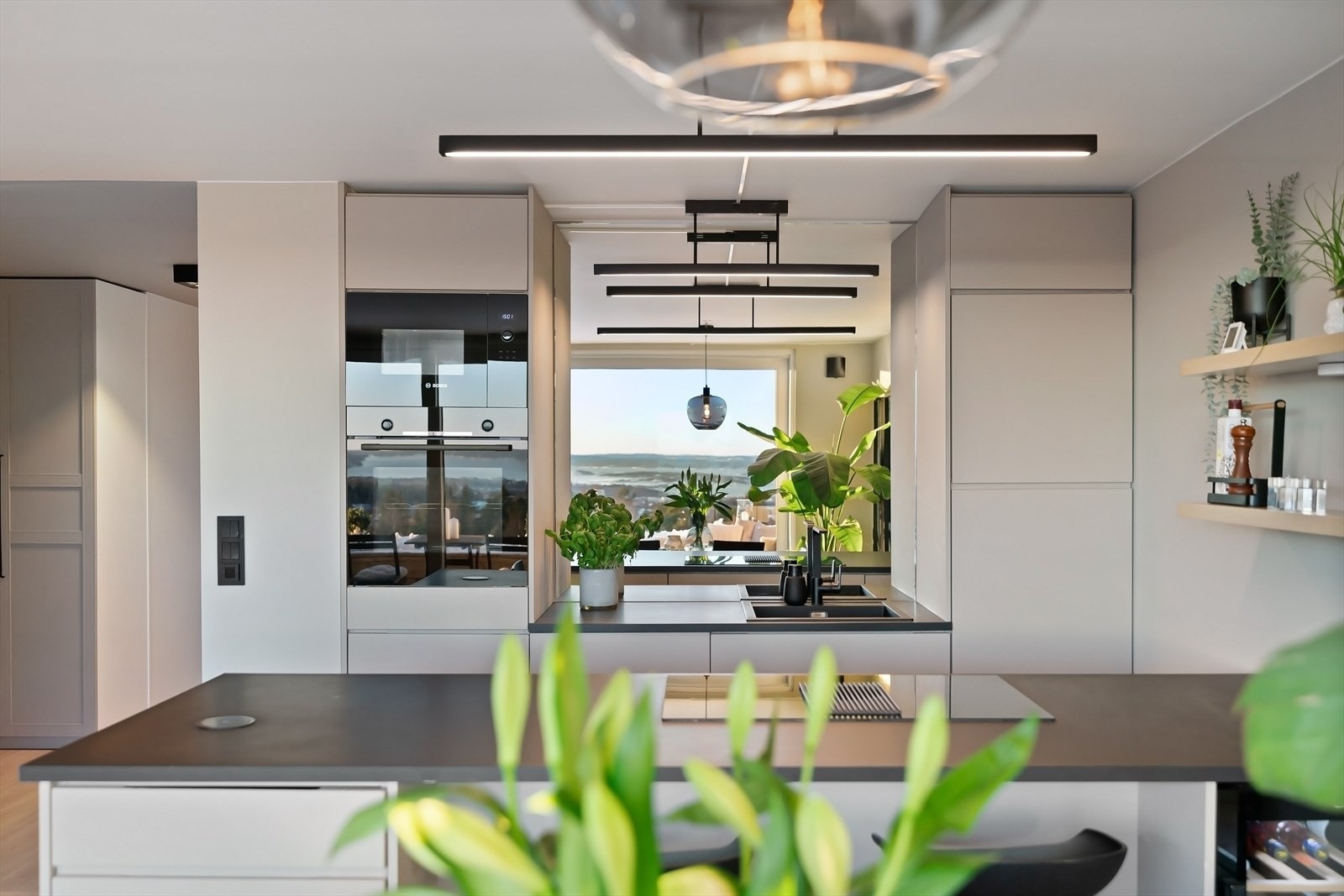 Kjøkkeninnredning med glatte fronter, speil på veggen over benkeplaten og laminat benkeplate med nedfelt kum. Galleribilde