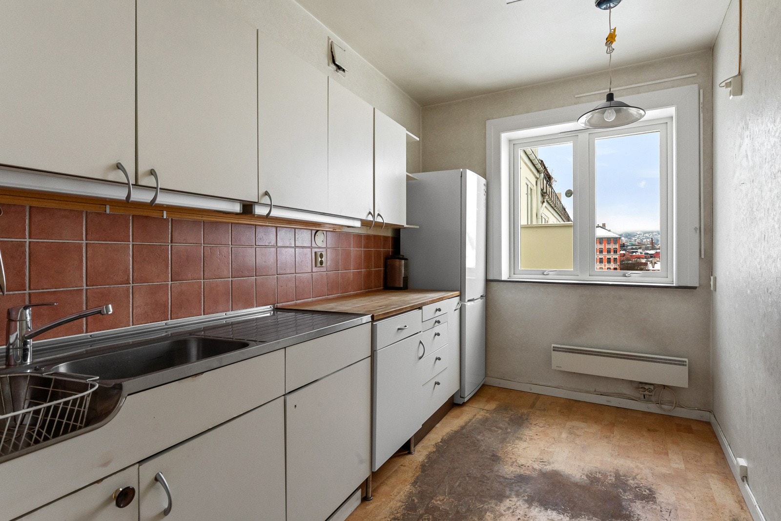 Eldre kjøkkeninnredning med hvite, folierte fronter og heltre benkeplate med heldekkende benkebeslag i rustfritt stål. Galleribilde