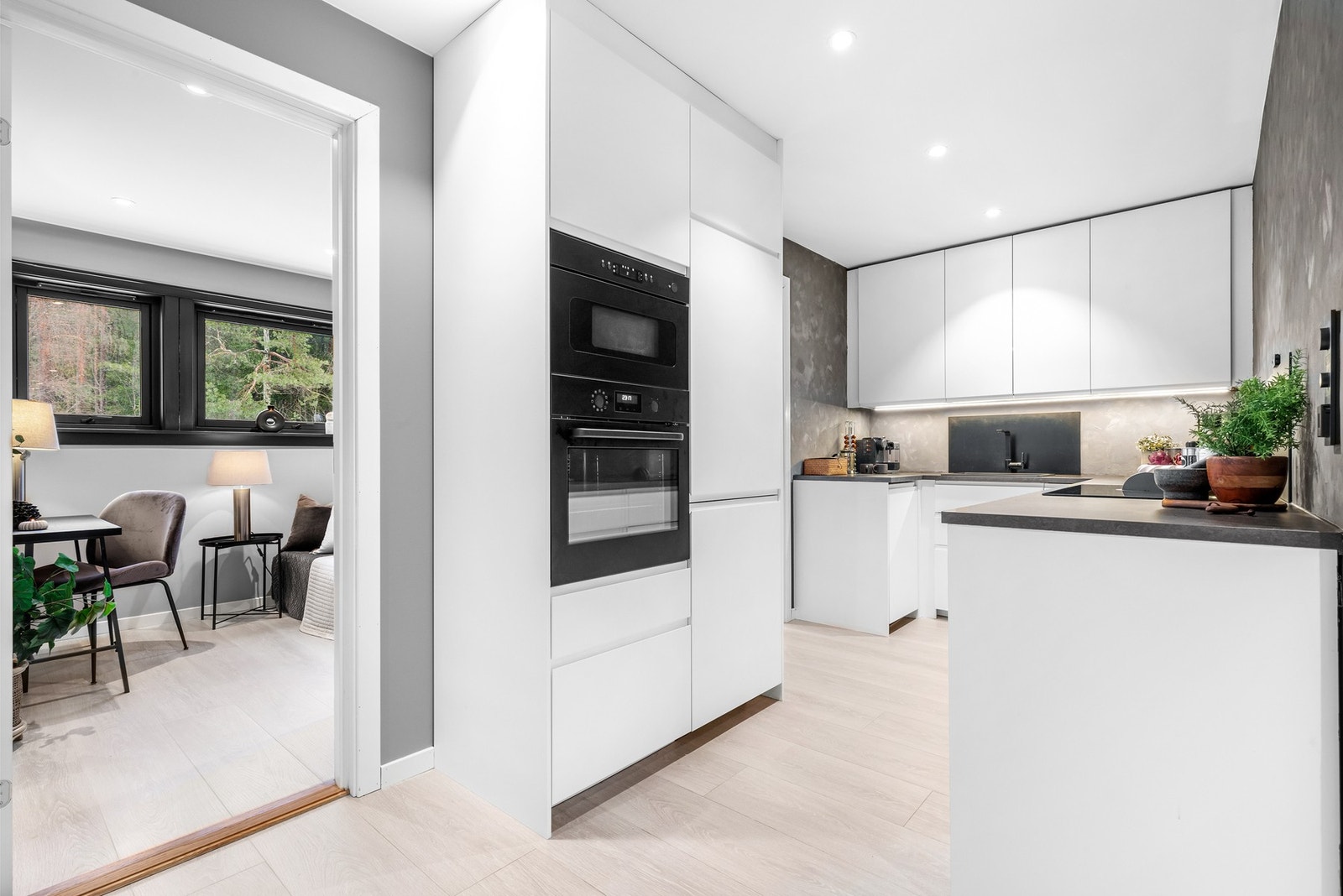 Glatte hvite fronter, mørk benkeplate, sort nedfeldt oppvaskum, sort blandebatteri og ledlys under overskap Galleribilde