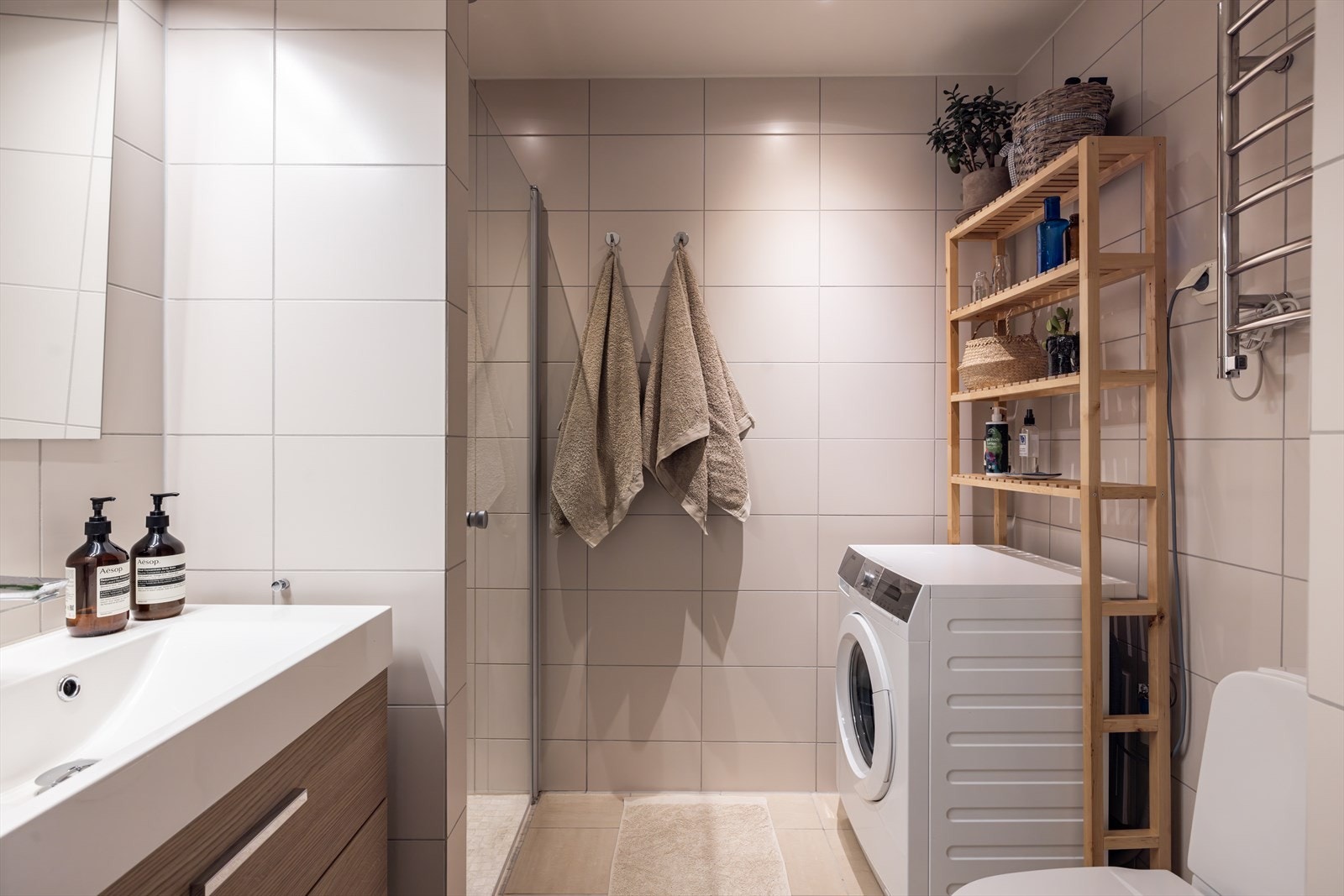 Delikat og moderne flislagt bad med varmekabler, downligths i taket og opplegg for vaskemaskin. Galleribilde