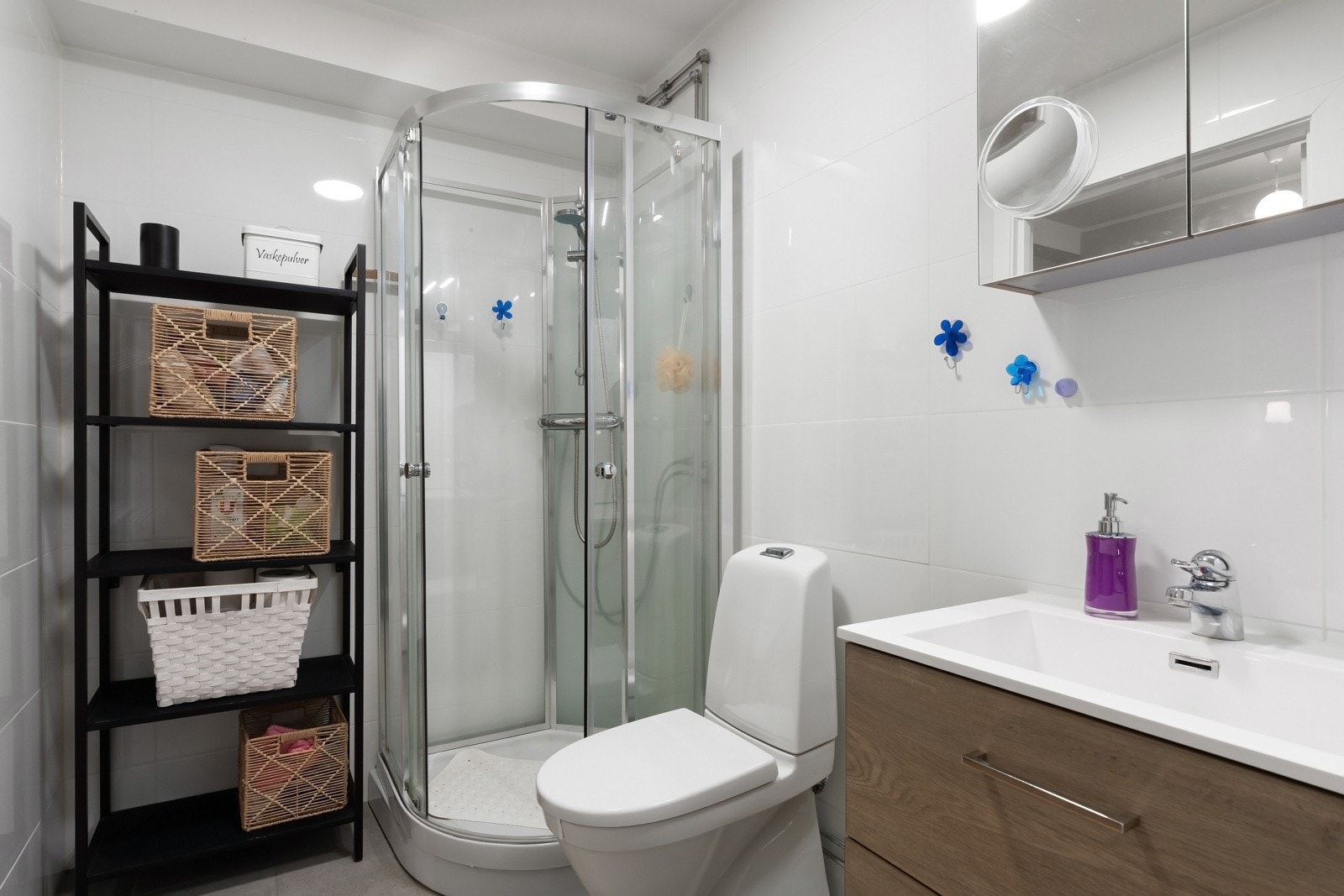 Baderomsinnredningen består av toalett, dusjkabinett, servant over innredning og speilskap på vegg. Galleribilde