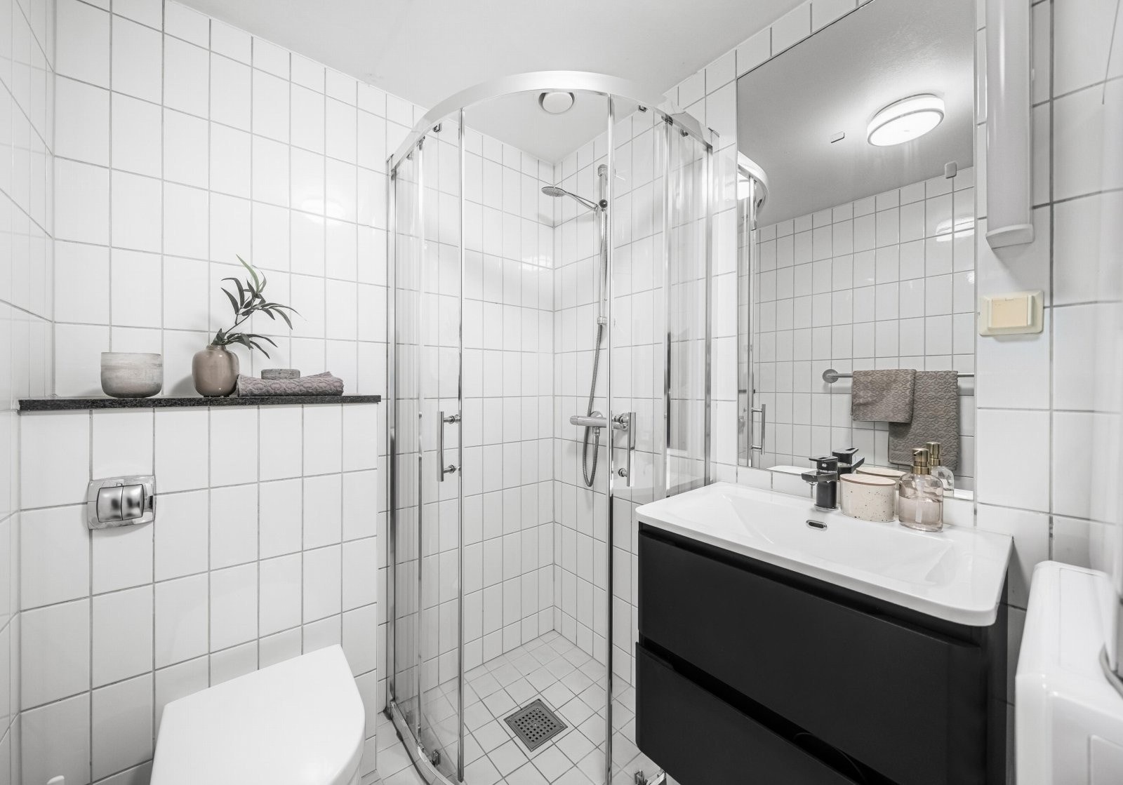 Badet er innredet med vegghengt toalett, dusjhjørne, servant med underskap og veggmontert speil. Galleribilde