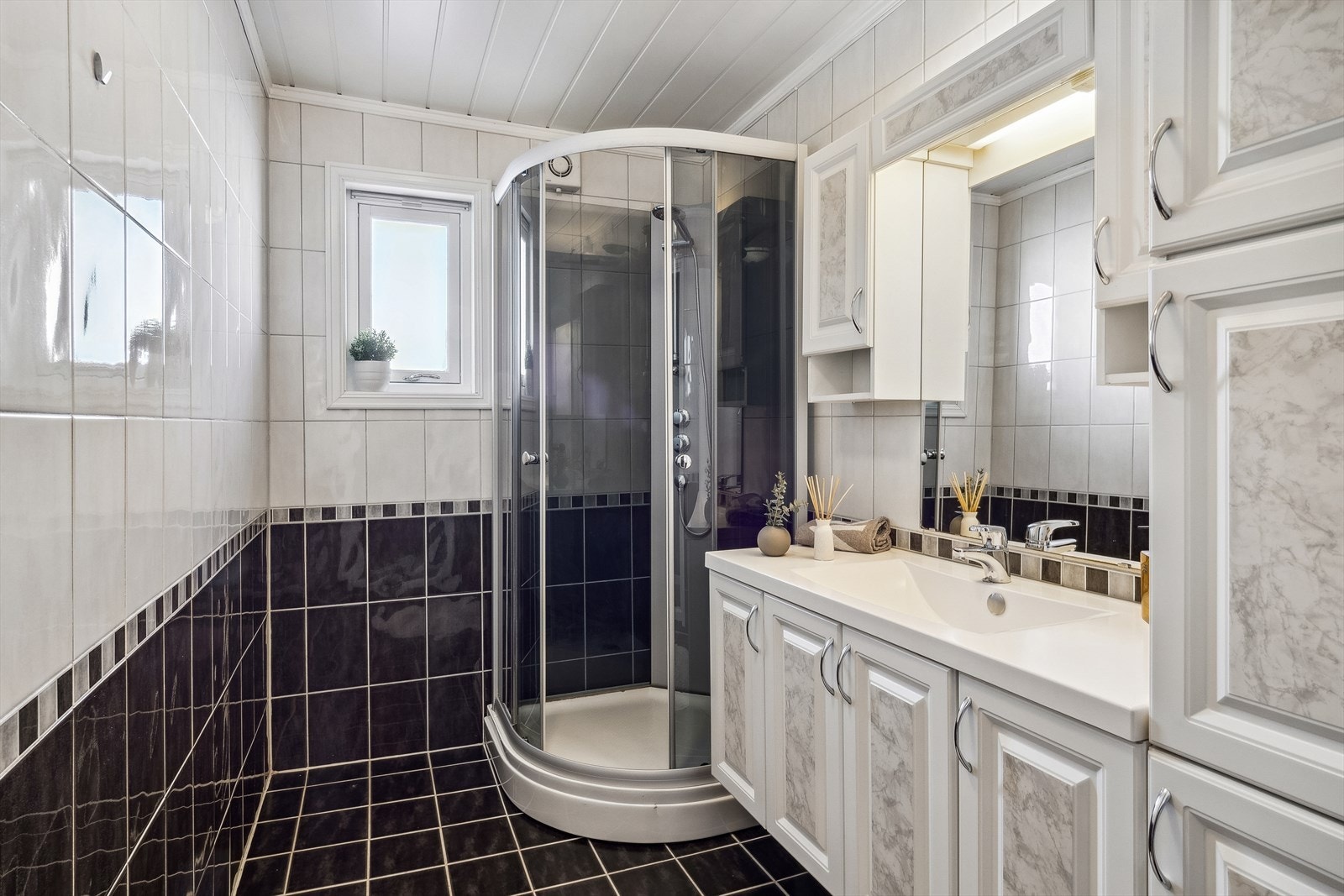 Bad med fliser på vegger og gulv med gulvvarme. Selger opplyser om ujevn varme fra dør på gulv så noen kabler er nok ute av drift nå. Rommet har innredning med servant, skap og dusjkabinett. Galleribilde