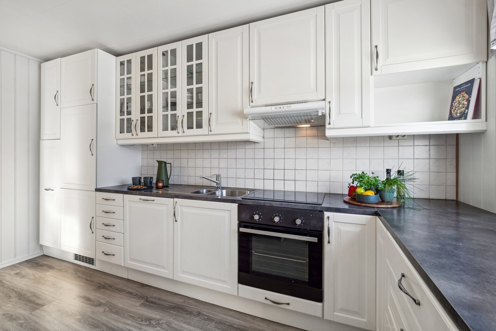 Pent kjøkken med hvite profilerte fronter og laminat benkeplate. Galleribilde