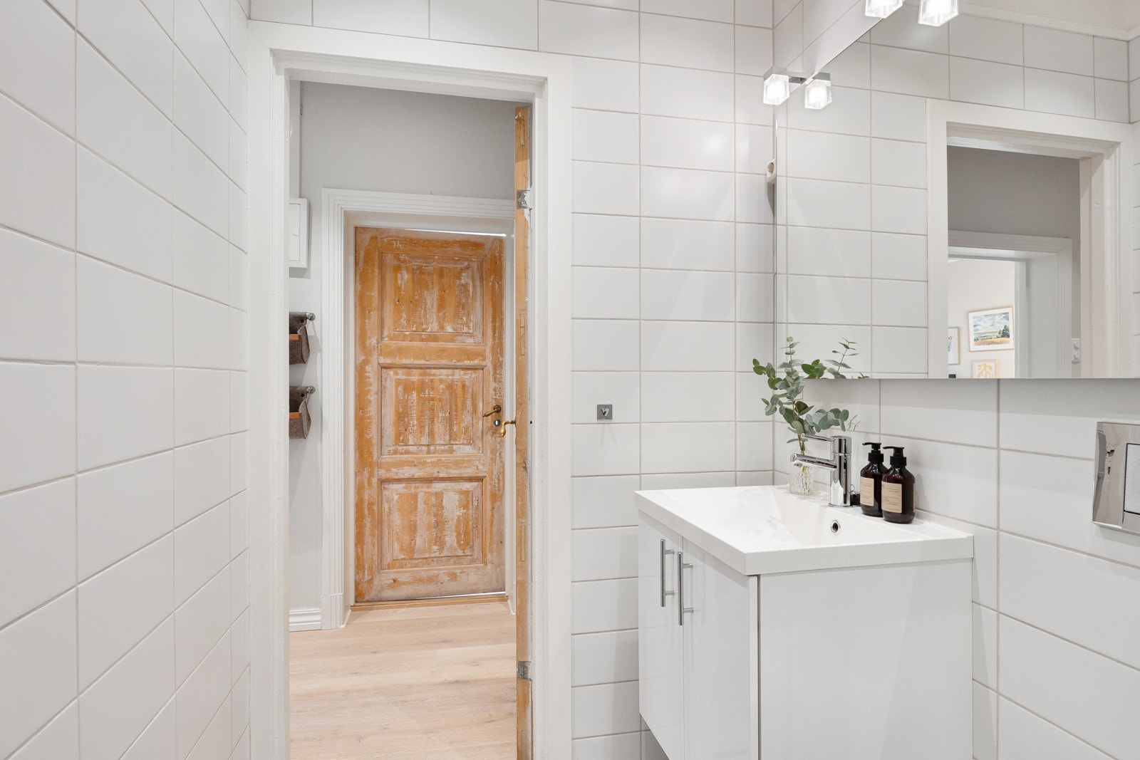 Flislagt bad fra 2010 med god belysning, speil, veggskap, hvit servantinnredning, dusjhjørne og veggmontert toalett. Galleribilde