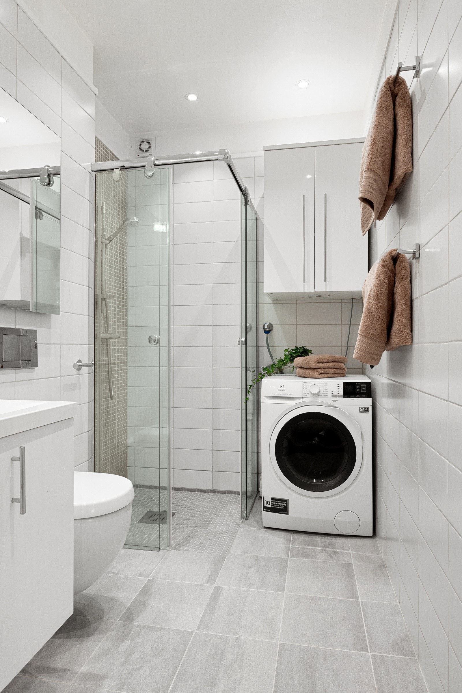 Badet har fliser på gulv og vegger, gulvvarme og downlights. Innredningen er lys og toalettet er veggmontert. Galleribilde