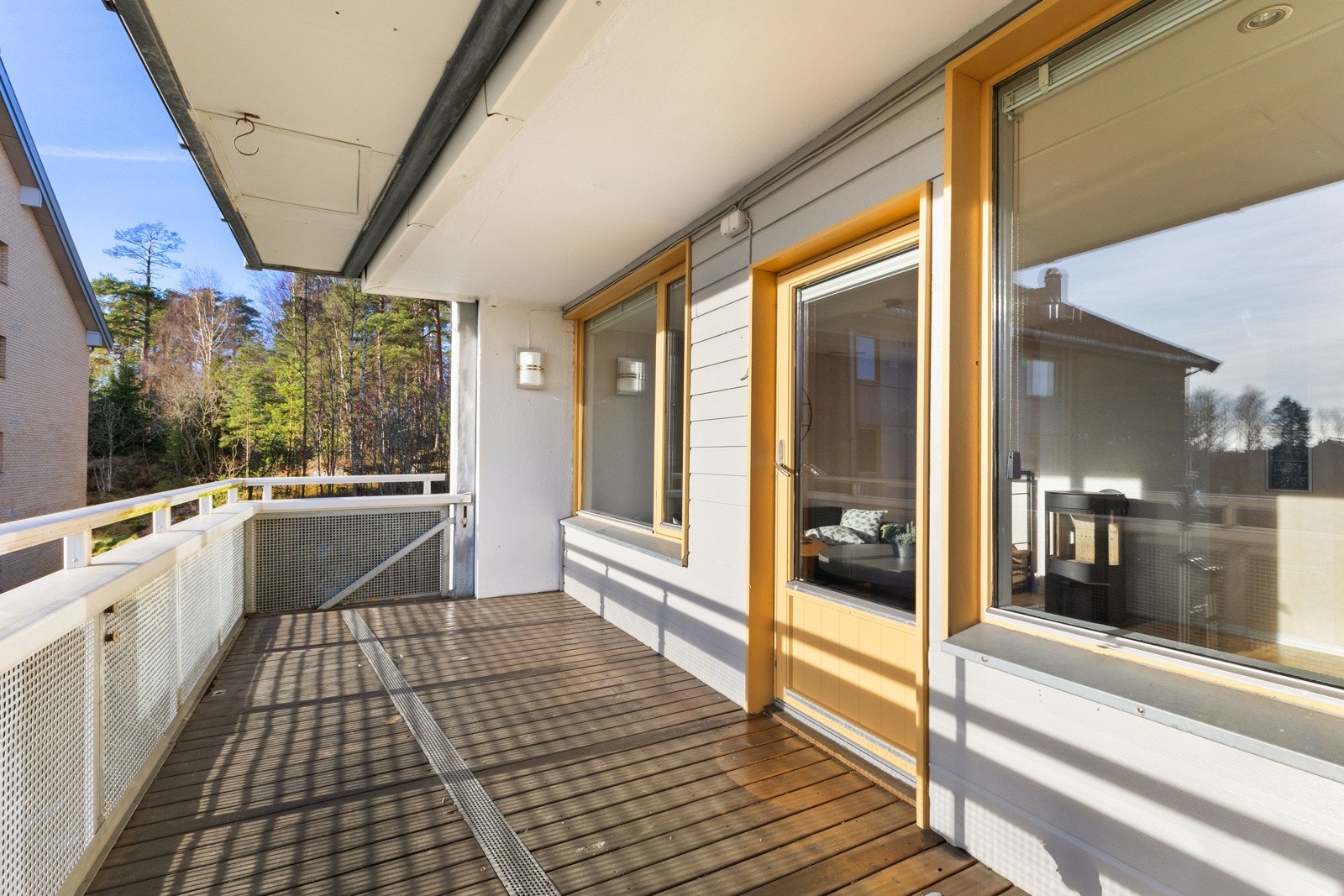 Romslig balkong med tregulv og hvitt rekkverk. Store vinduer gir godt lysinnslipp til stuen. Utsikt mot skogsområde gir en følelse av ro og privatliv. Galleribilde