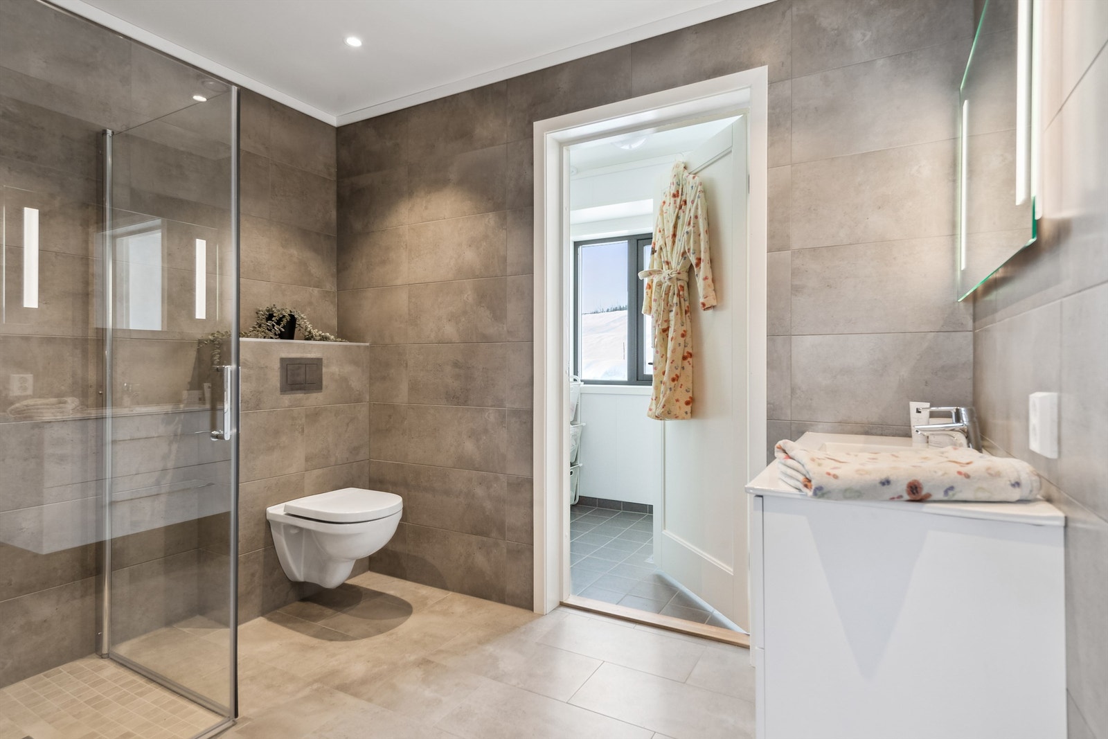 Velkommen til Starumsvegen 56 - Delikat bad i 1. etasjen med fliser på gulv og vegger, dusj, vegghengt toalett og servant. Rommet innbyr til en god start på dagen. Galleribilde