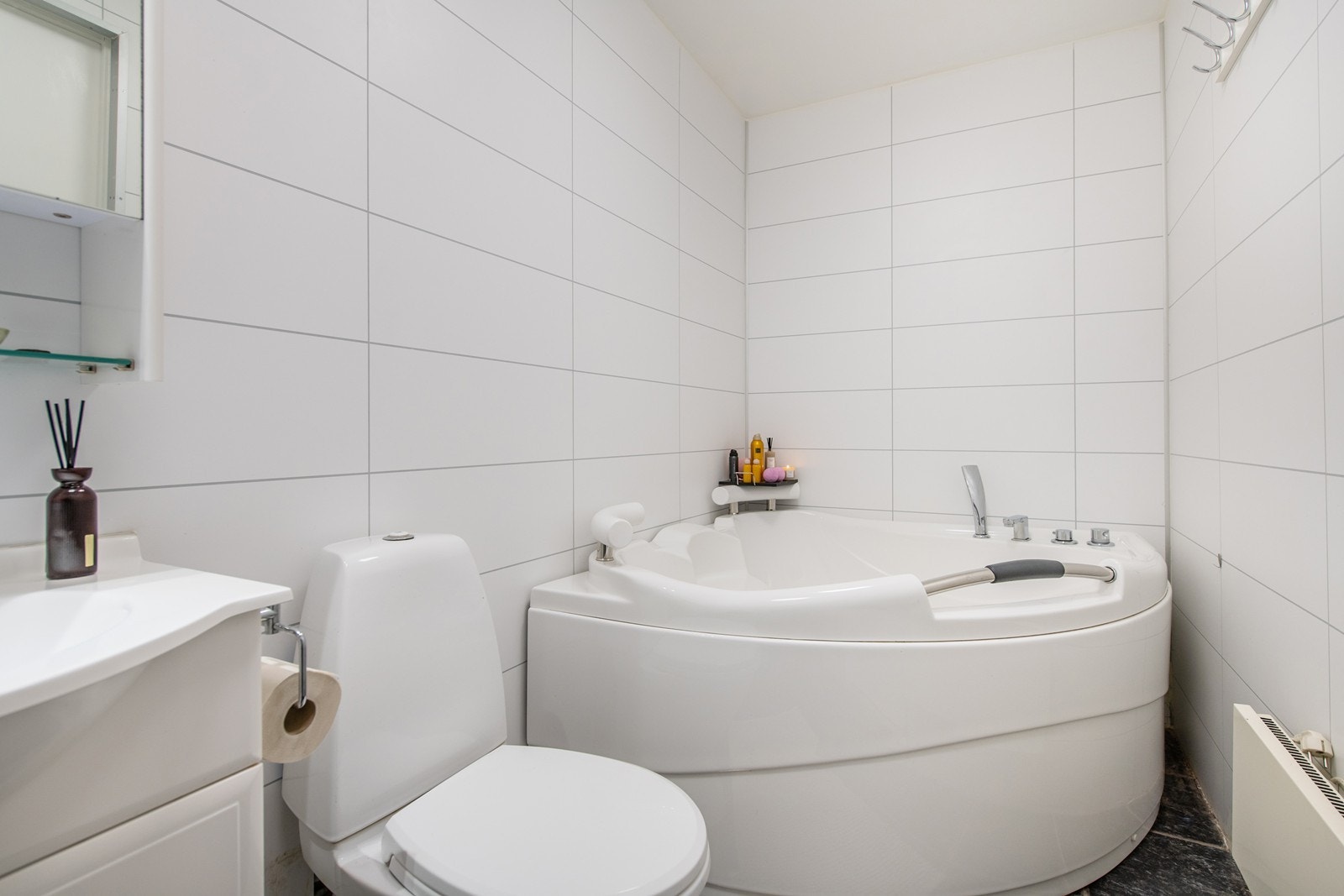 Badet har fliser på gulvet og malte vegger og tak av malt betong. Det er utstyrt med et hjørnebadekar, servant med skapinnredning, opplegg for vaskemaskin og toalett Galleribilde