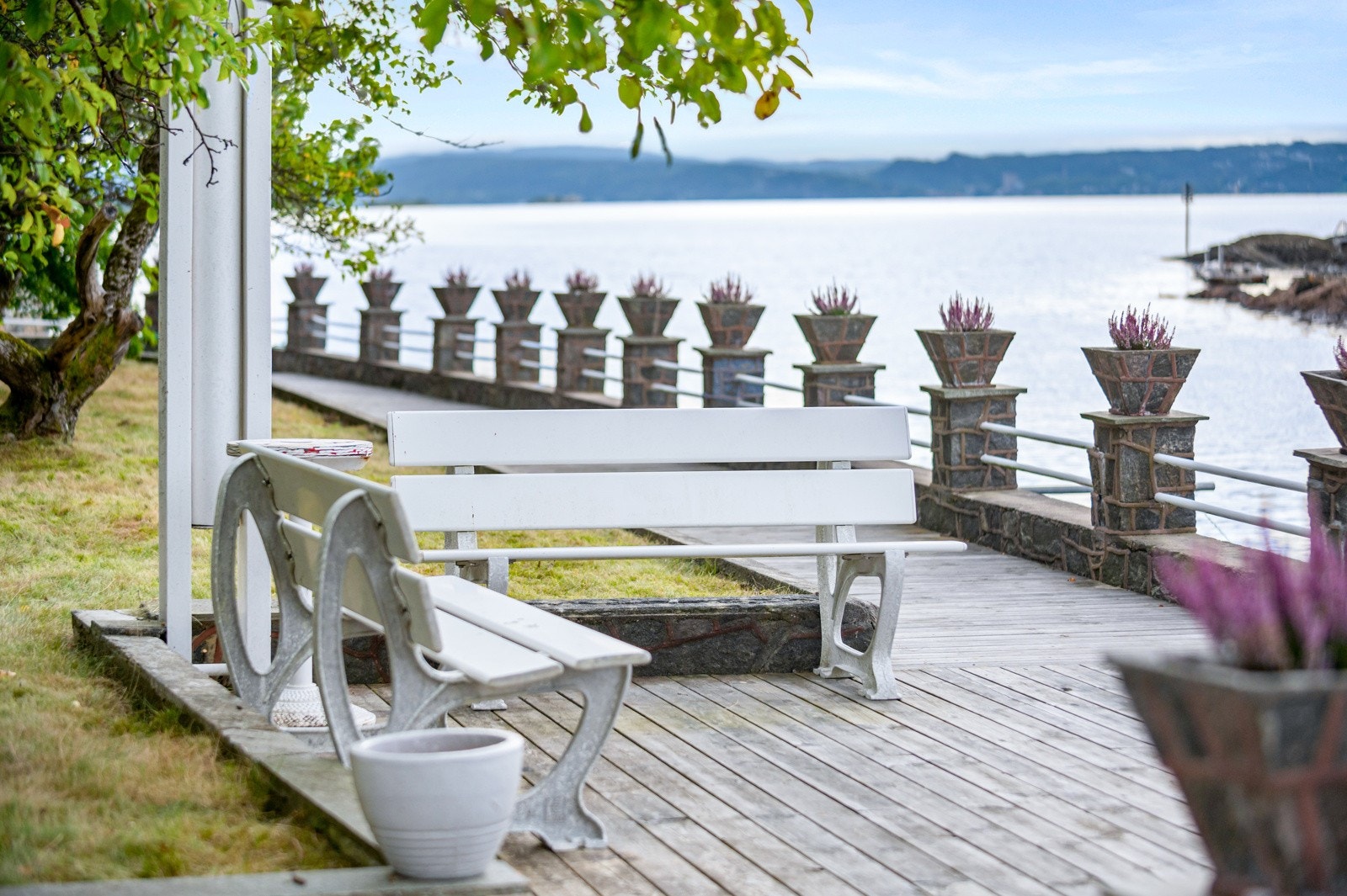 Tomten er opparbedeidet med store plenarealer, oppmurt steinkant, skiferplattinger, treplatting og oppmurte blomsterpotter langs hele tomtens bredde mot sjøen. Galleribilde