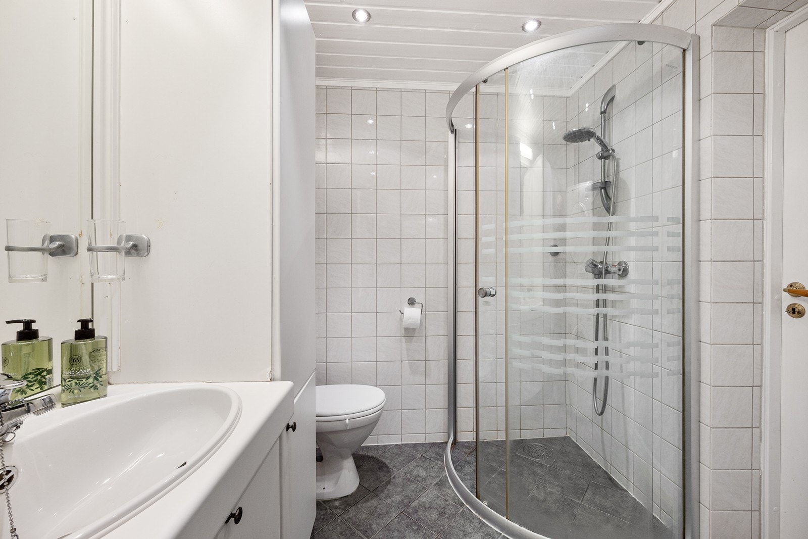 Baderomsinnredningen har hvite, glatte skapfronter, to høyskap, samt heldekkende servant og speil med belysning. Galleribilde