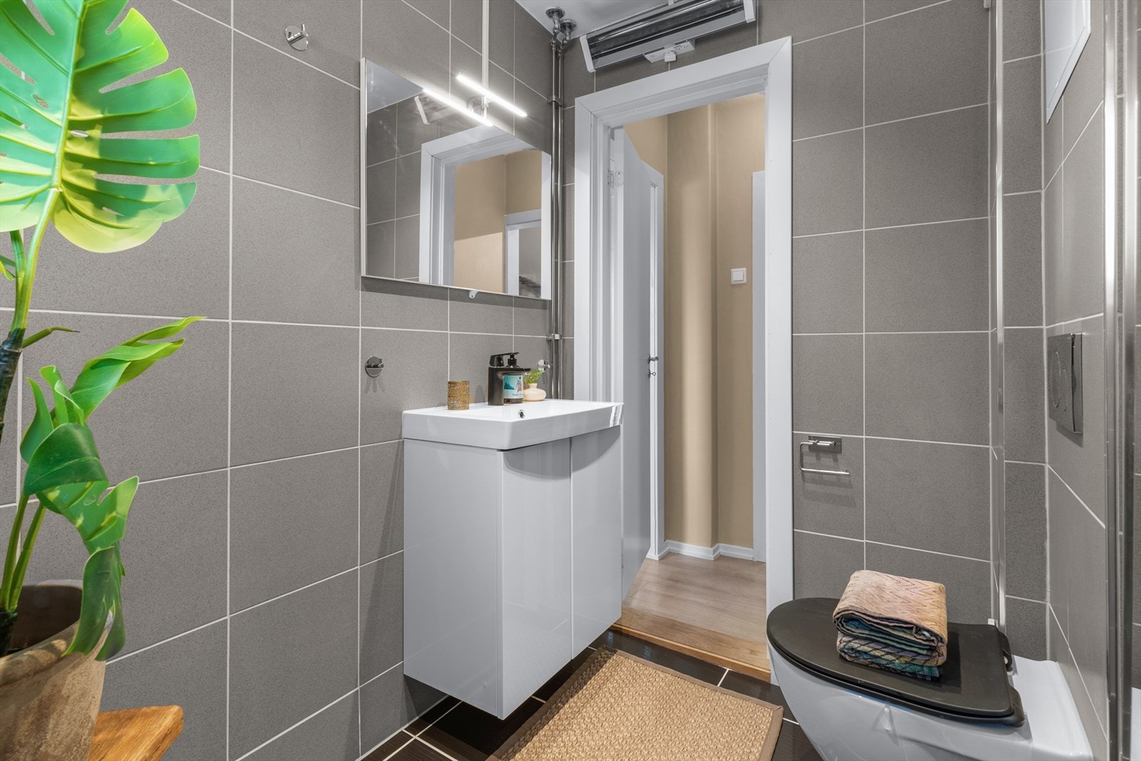 Badet er utstyrt med skap med heldekkende servant, speilskap, høyskap, veggmontert toalett og dusjsone med regnfalldusj Galleribilde