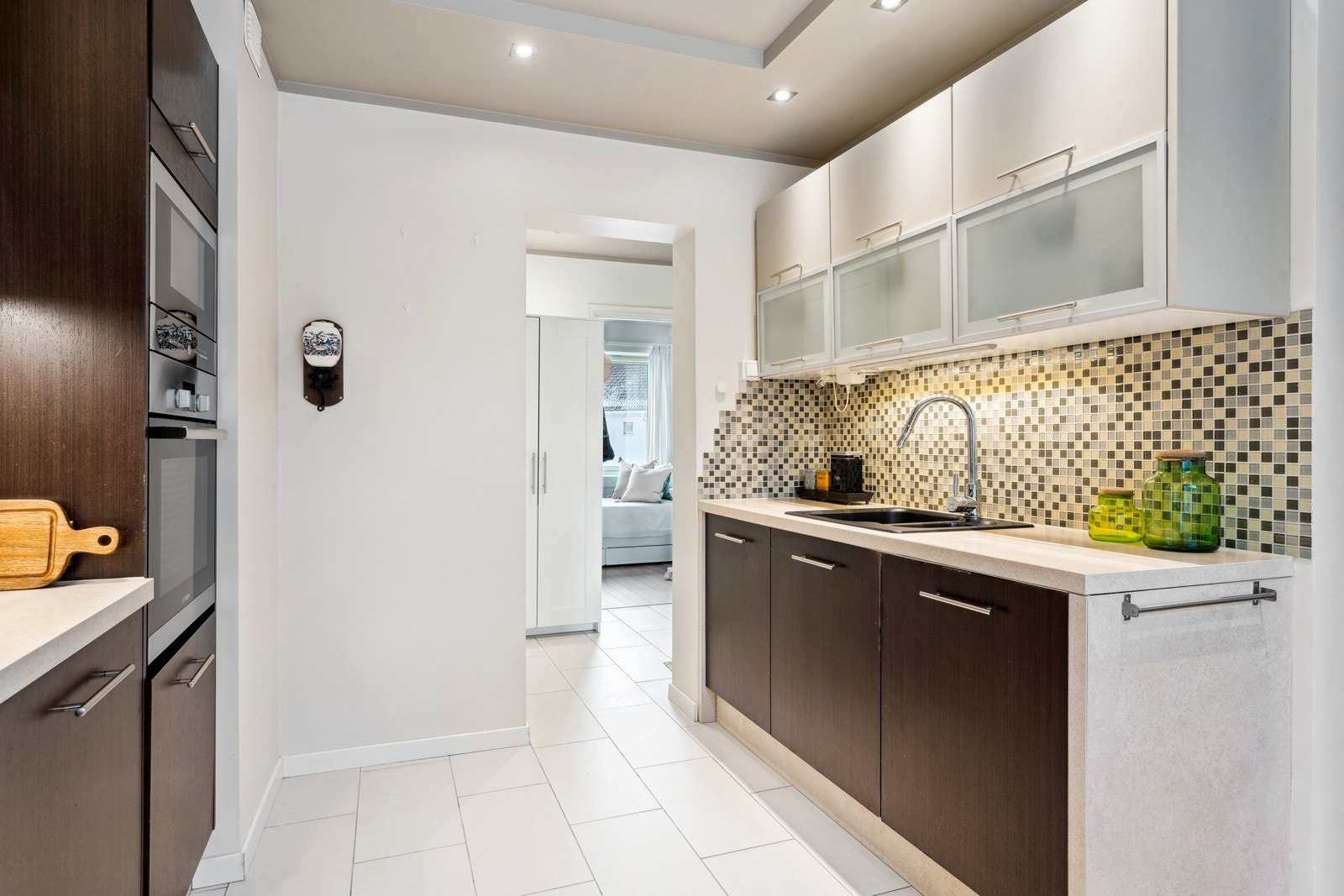 Kjøkkeninnredning med glatte fronter og laminert benkeplate. Flislagte vegger mellom benkeplate og overskap, overskapsbelysning og stikkontakter. Galleribilde