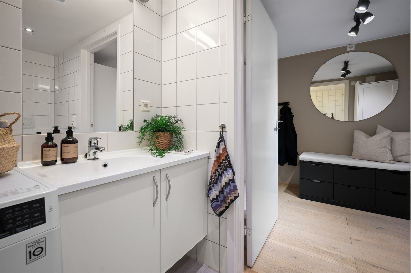 Bred heldekkende servant med skapinnredning og speil med belysning over samt opplegg for vaskemaskin og tørketrommel Galleribilde