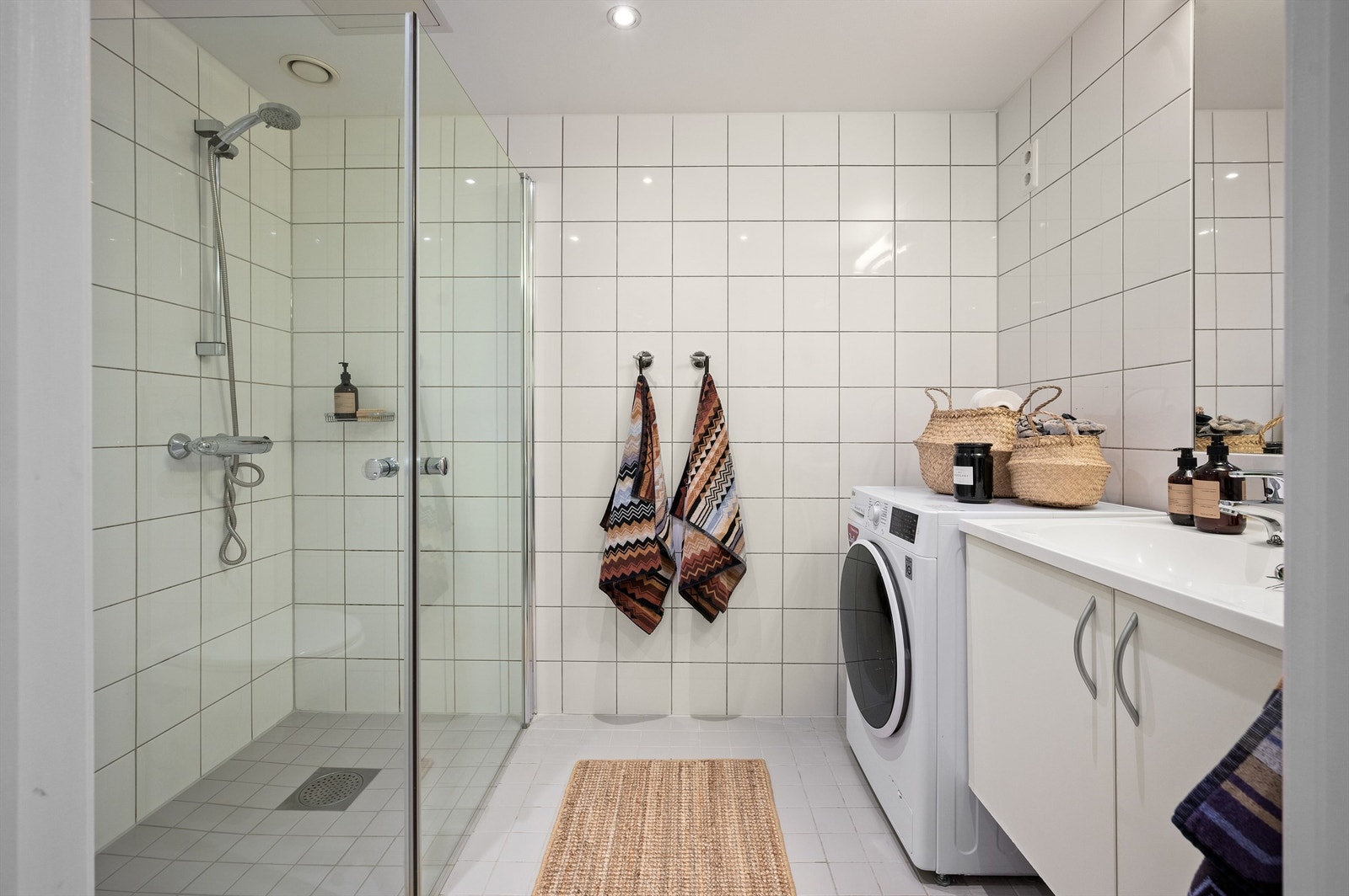 Pent og meget romslig bad med lyse, grå fliser på gulv, hvite veggfliser og downlights i himling samt varme i gulv Galleribilde