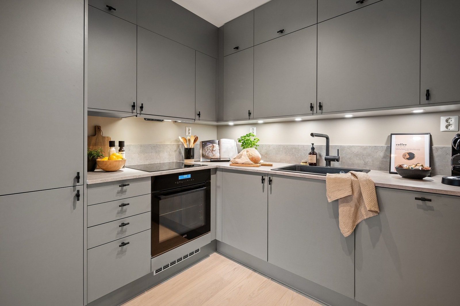 Her er det innredning med grå fronter, laminat benkeplate og backsplash, nedfelt oppvaskkum og ett-greps armatur, begge i sort utførelse Galleribilde