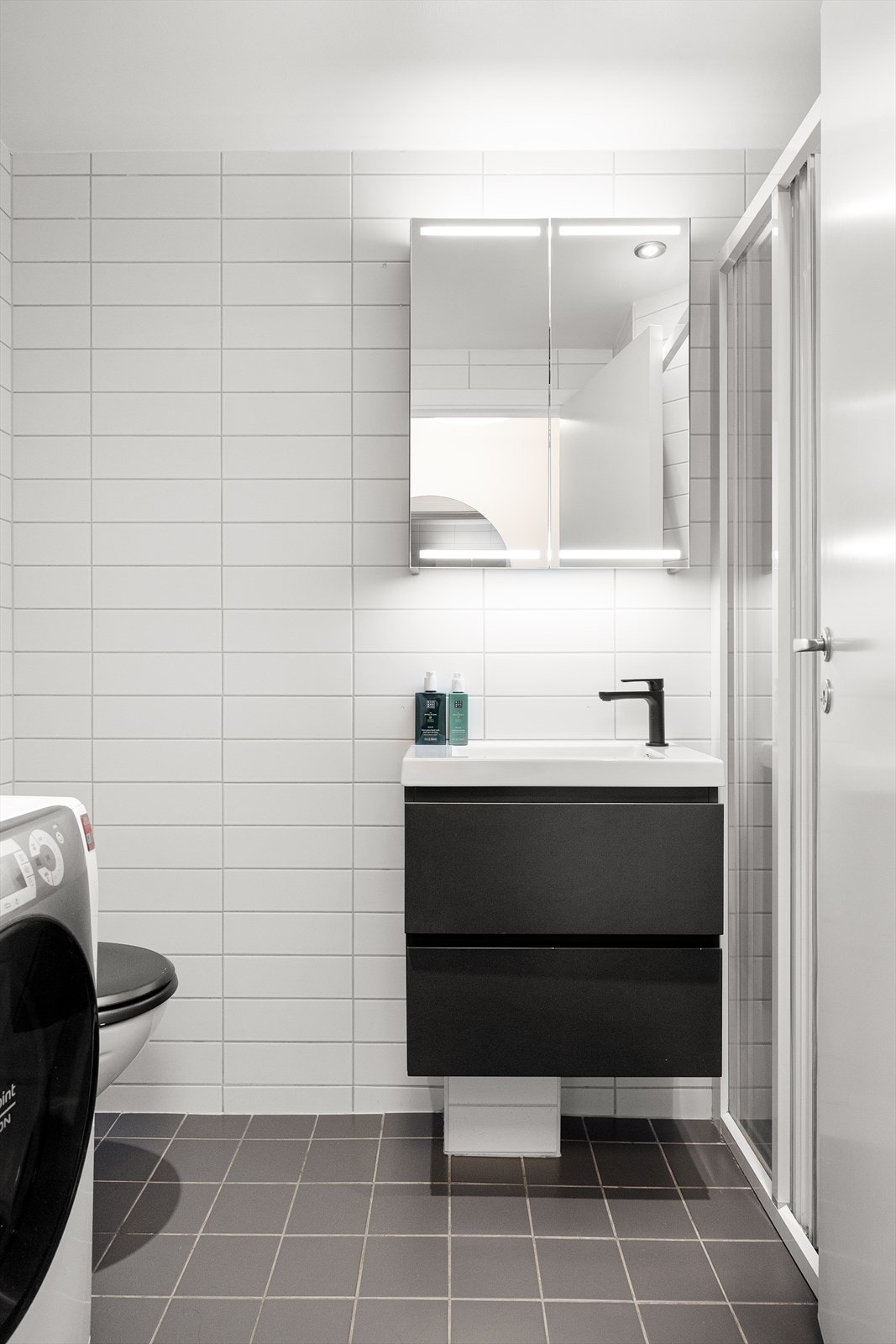 Flislagt bad med behagelig gulvvarme, baderomsinnredning med skuffer, servant og speil, dusjnisje og veggmontert toalett. Galleribilde