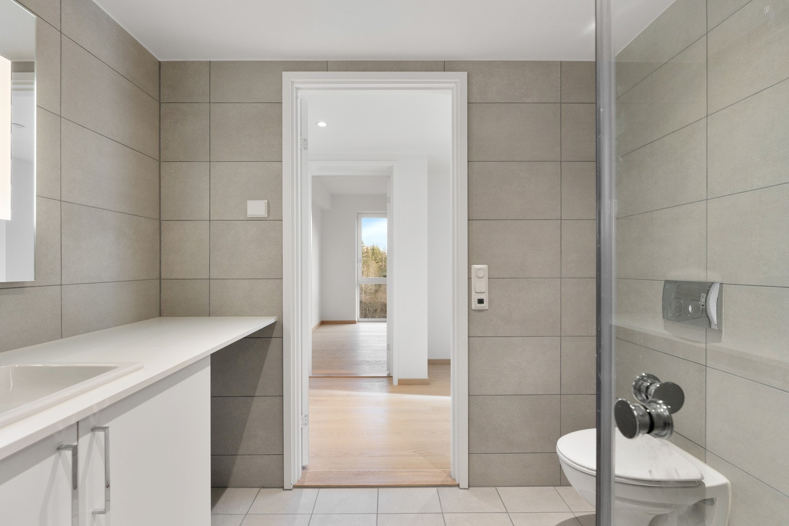 Delikat flislagt bad med vegghengt toalett, dusjsone med innfellbare dører samt servant med skapinnredning. Galleribilde