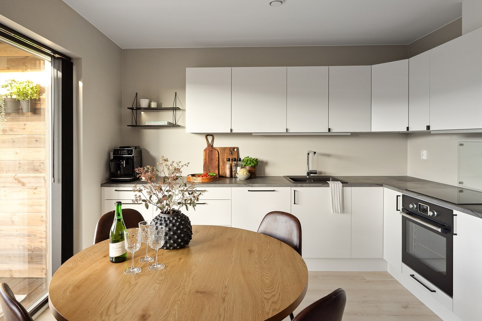 Kjøkkenet fra Sigdal er delvis integrert med innredning og benker langs to vegger. Skapfronter og skuffer er hvite med elegante håndtak, mens benkeplaten kommer i marmorert grå - en tiltalende kombinasjon. Galleribilde