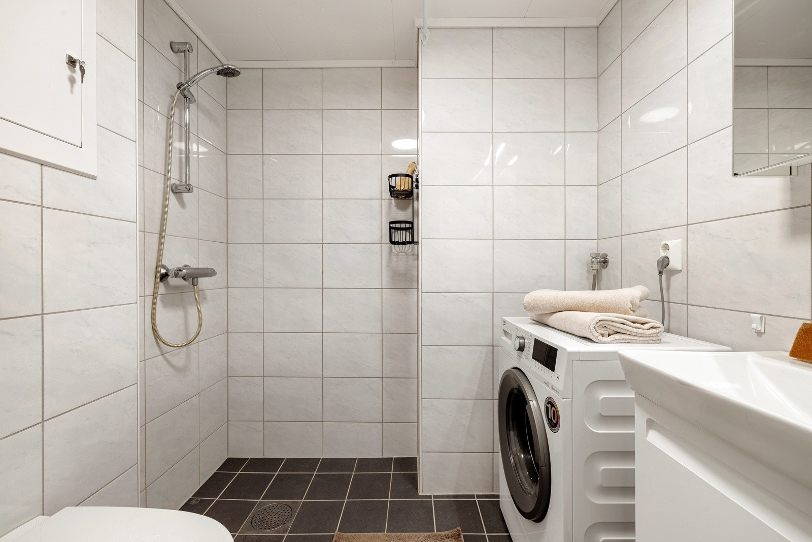 Badet har moderne møblement og et praktisk speilskap. Videre er badet innredet med dusj, vegghengt toalett og opplegg for vaskemaskin. Galleribilde