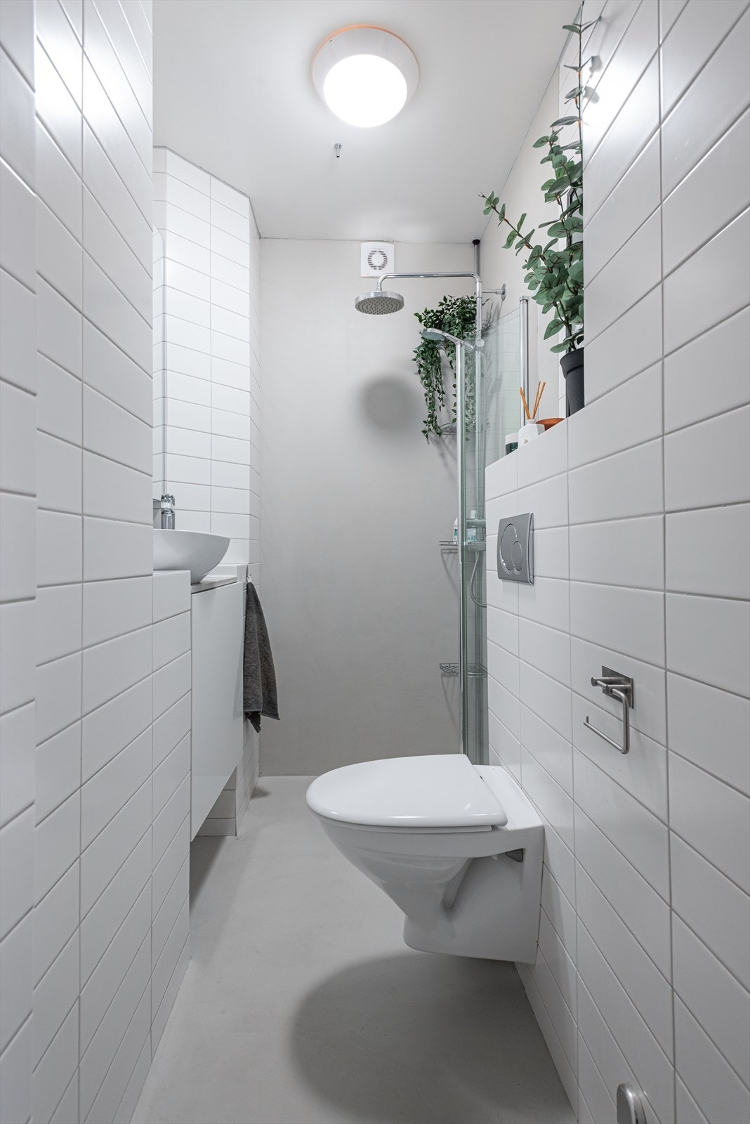 Overflateoppusset bad fra 2022 med fliser og mikrosement med innredning bestående av flislagt hylle, innebygd sisterne og benkskap med glatte fronter. Galleribilde