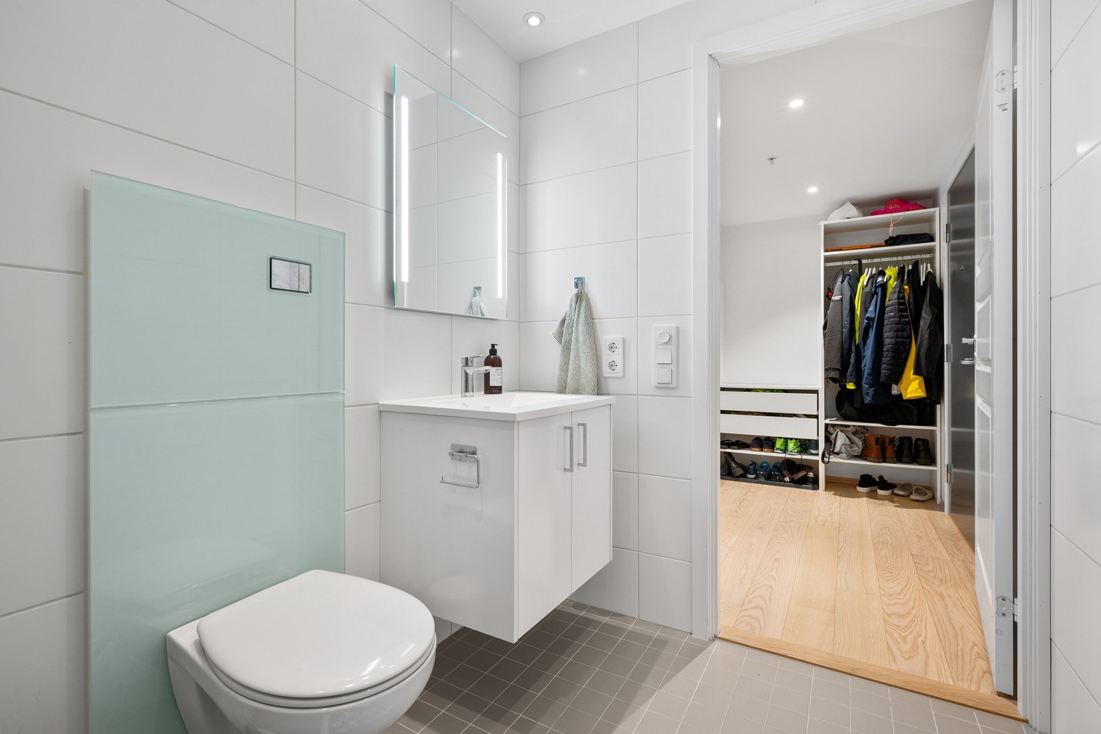 Badet er innredet med 2 dusjdører i glass, kran og avløp for vaskemaskin, samt servant på underskap og speil med lys. Galleribilde