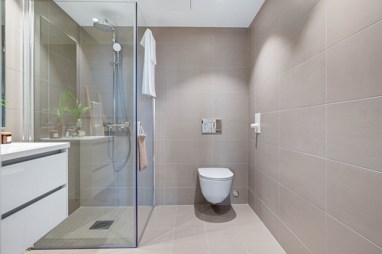 Badet består av vegghengt wc, dusjsone med innfellbare dusjdører og fossefalldusj, samt servant i hvit skuffeseksjon. Galleribilde