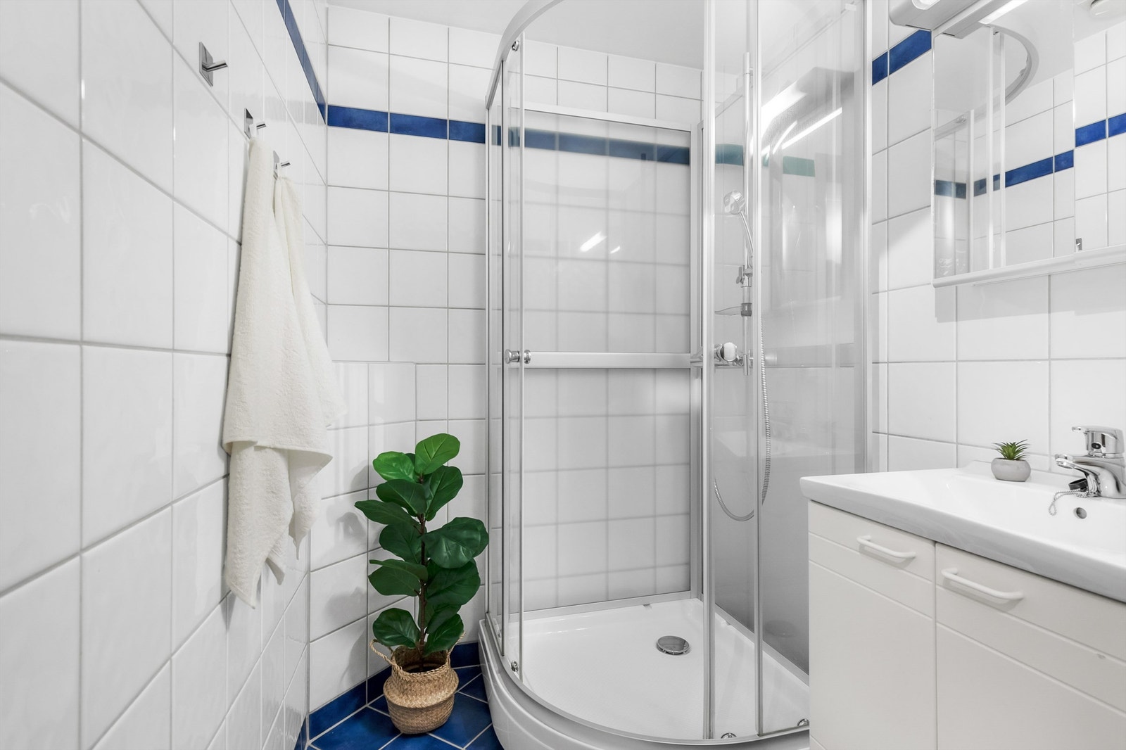 Boligens bad er flislagt på gulv og vegger med varme i gulvene. Badet er innredet med vegghengt servantskap og servant, speilskap med overlys og dusjkabinett med skyvedører i glass. Galleribilde