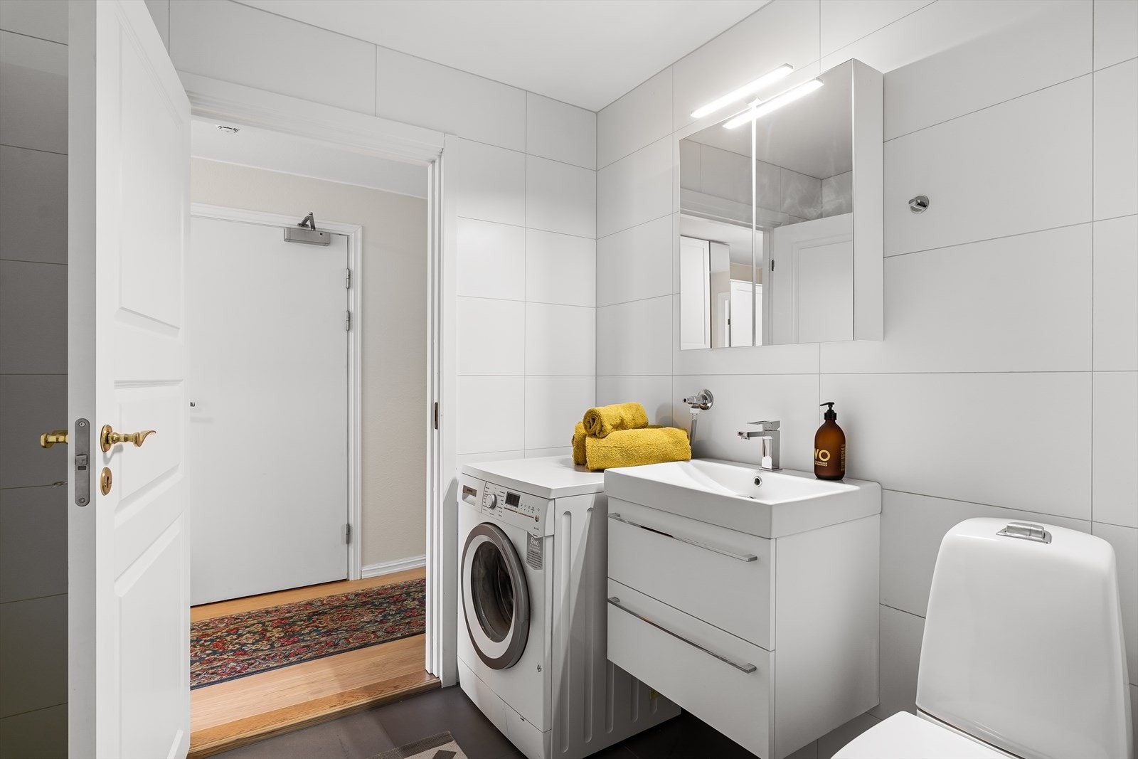 Badet er utstyrt med servant med underskuffer, speilskap med LED-lys, høyskap, gulvmontert toalett og opplegg for vaskemaskin/tørketrommel. Galleribilde