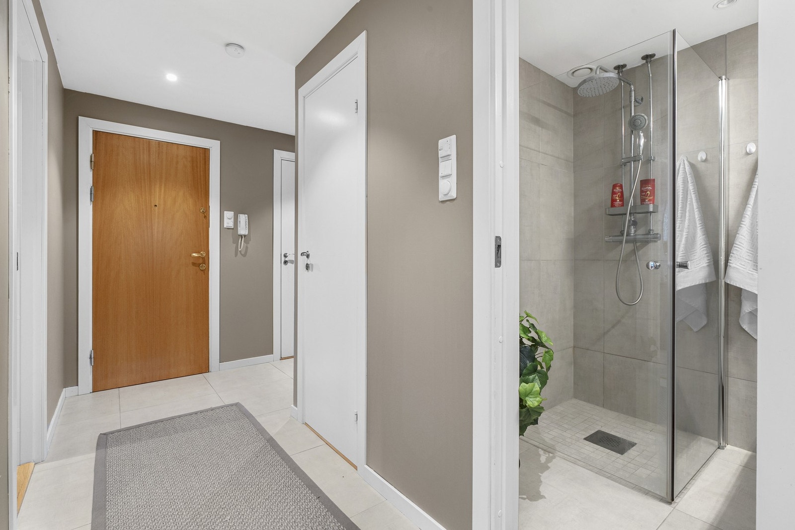 Entreen har lyse gulvfliser, gulvvarme, listefri himling med downlights og glatte vegger malt i en varm, gråbeige nyanse. Galleribilde