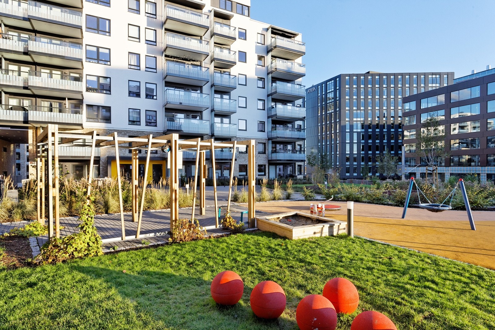 Pent opparbeidet fellesareal med sittegrupper og lekestativer, diverse busker og beplatninger. Galleribilde