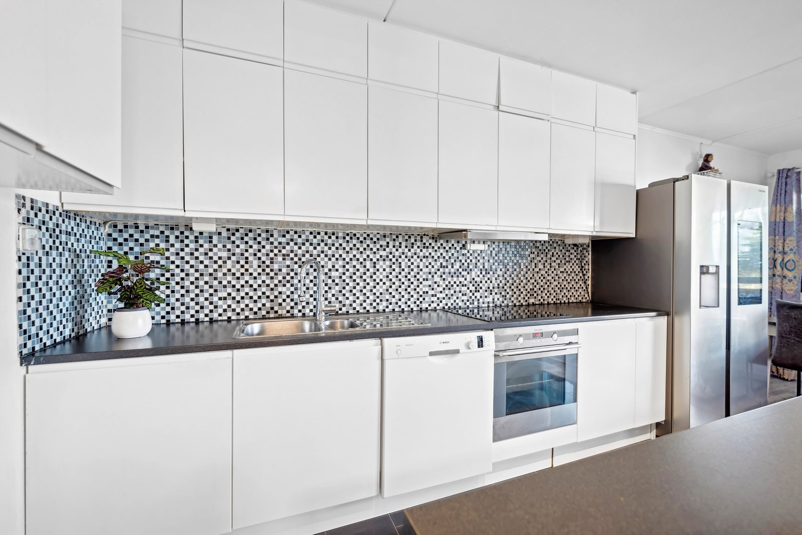 Kjøkkeninnredning med hvite glatte fronter, benkeplater i laminat, oppvaskkum, ventilator med kullfilter, opplegg for oppvaskmaskin og integrerte hvitevarer. Galleribilde