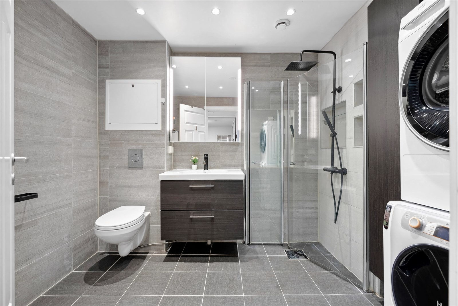 Bad med adkomst fra hall: Gulv- og veggflatene består av fliser. Veggmonterte dusjvegger, dusj direkte på gulv med termostat batteri, veggmontert dusjtoalett, servant med skuffer, speilskap med
belysning og opplegg for vaskemaskin. Galleribilde