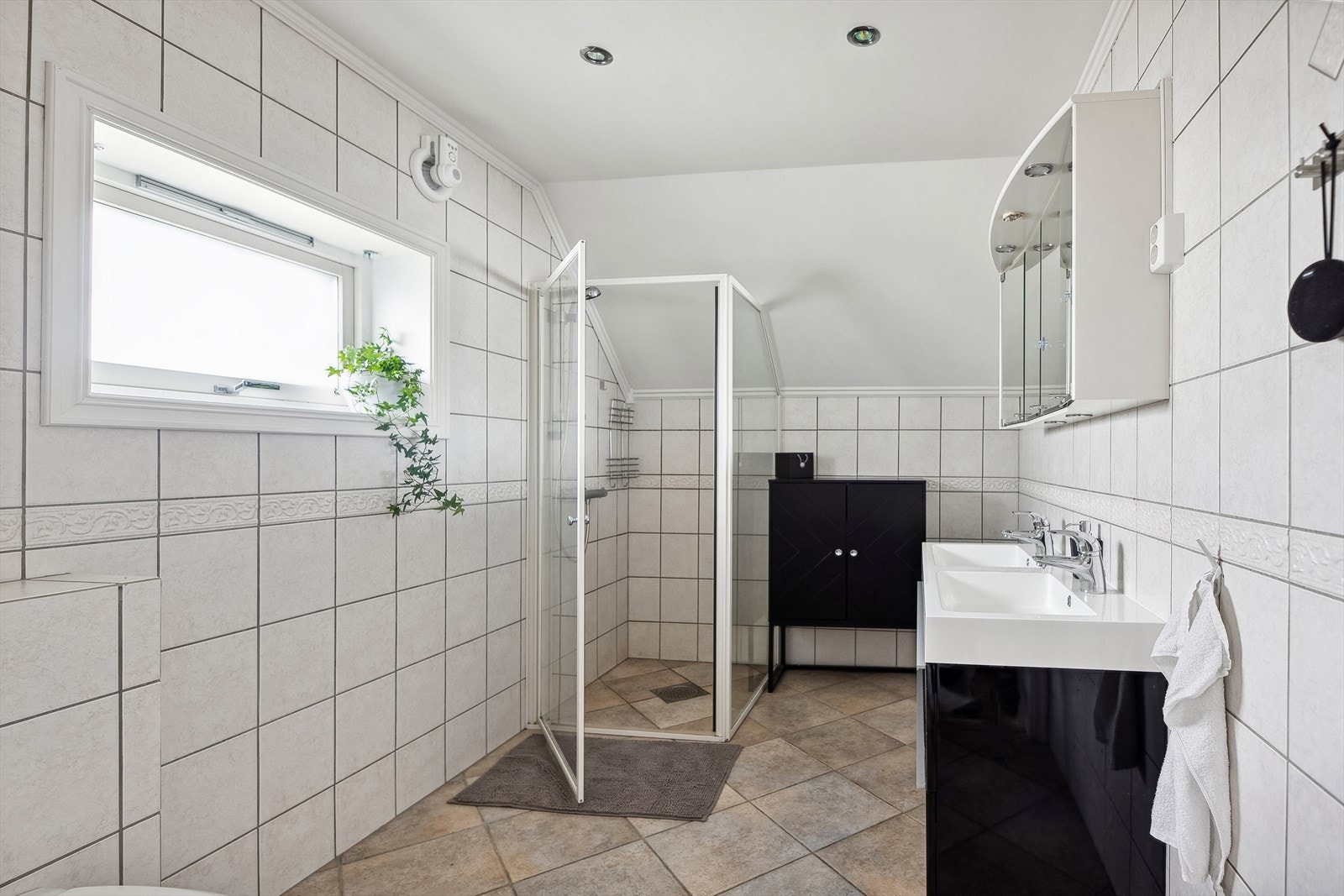 Flislagt baderom som er innredet med heldekkende dobbel servant, to blandebatteri, dusjhjørne og veggmontert toalett. Galleribilde