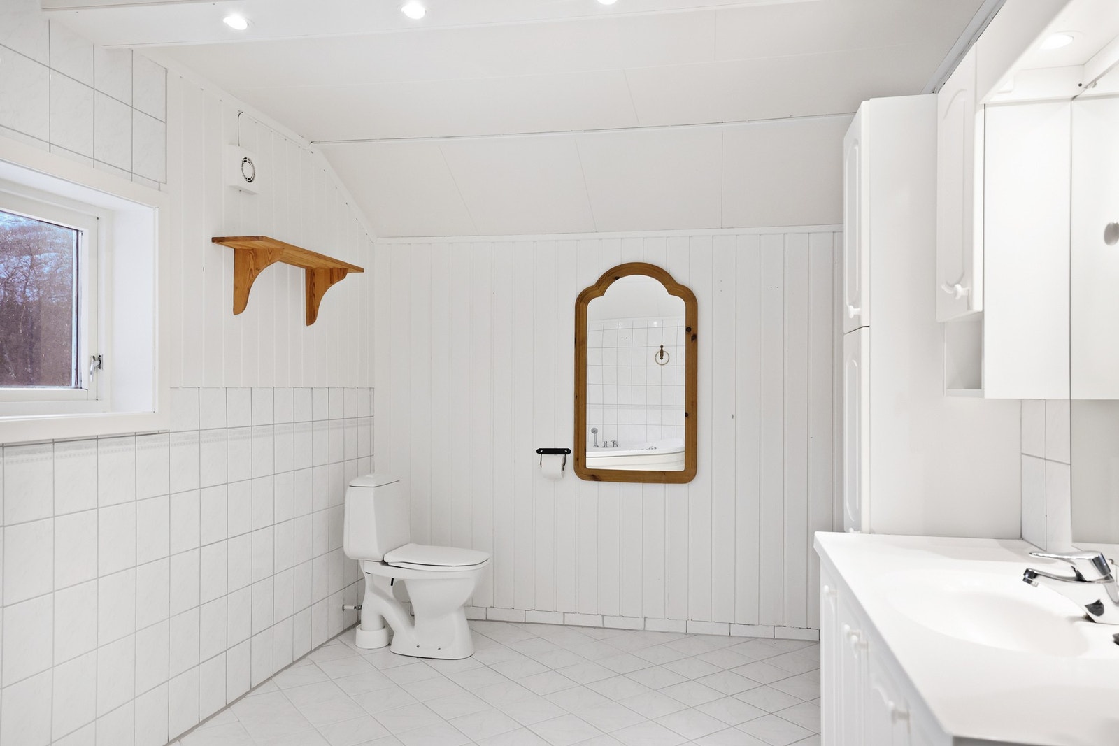Det er en romslig lys vegghengt servantinnredning med speil og overlys. Badet har et hjørnebadekar, Galleribilde