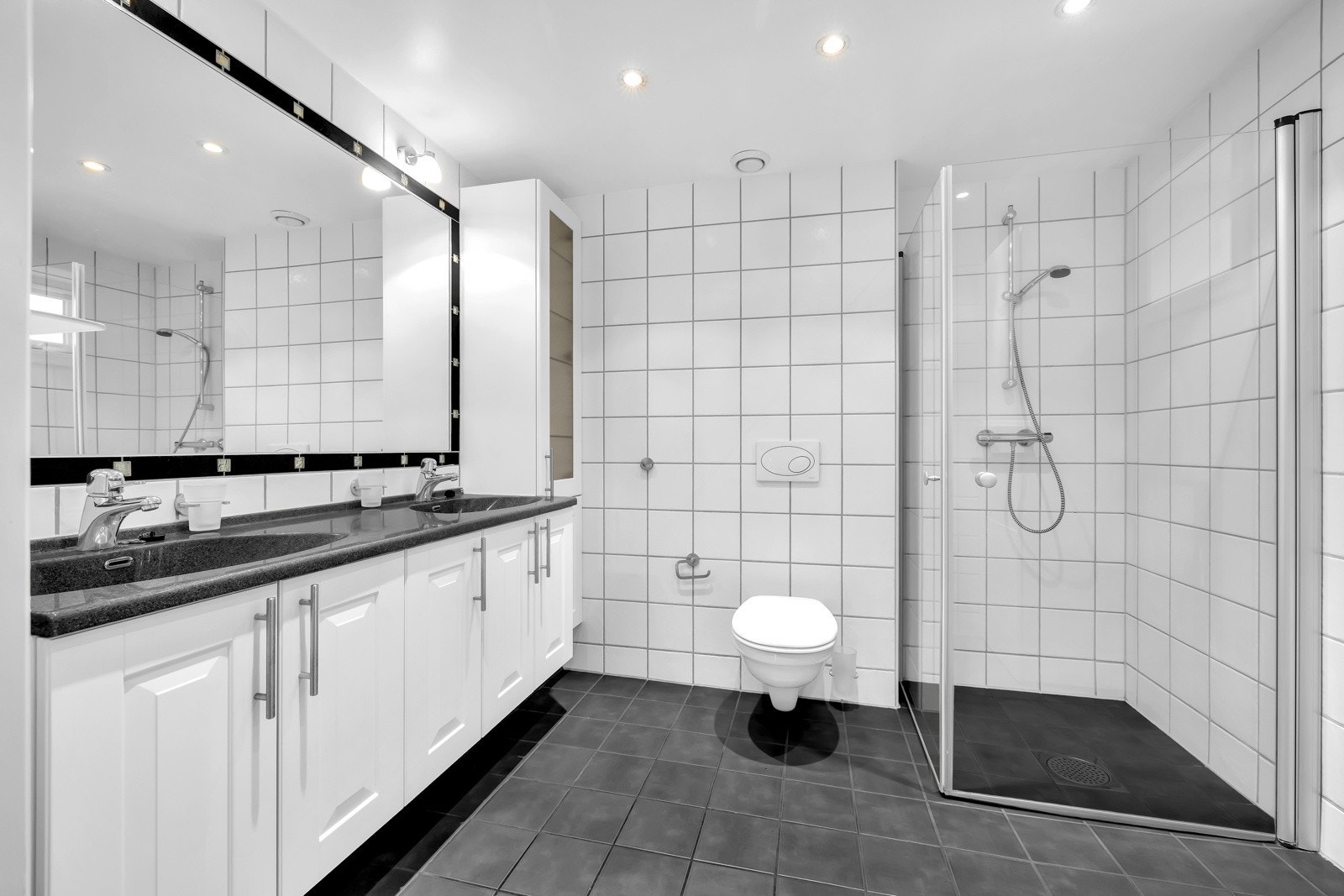 Baderom 1 er fra byggeår og har flislagt gulv med varme og flislagte vegger. Badet er utstyrt med nedsenket himling med malt flate og downlights og vegghengt servantskap med profilerte fronter. Galleribilde