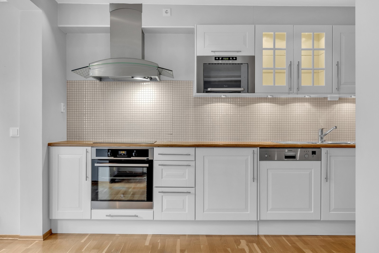 Videre har kjøkkenet fliser mellom benkeplate og overskap, benkeskapsbelysning og stikkontakter under overskap, samt vegghengt ventilator med mekanisk avtrekk. Galleribilde