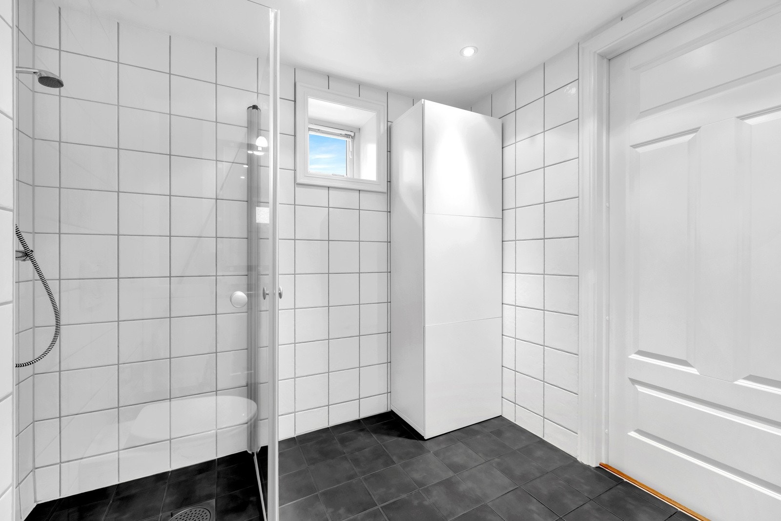 Videre er badet utstyrt med nedsenkede servanter med ett-greps armatur, vegghengt speil med overbelysning, dusjhjørne med innfellbare glassdører og dusjarmatur tilkoblet hånddusj, samt vegghengt toalett med innebygget sisternekasse. Galleribilde