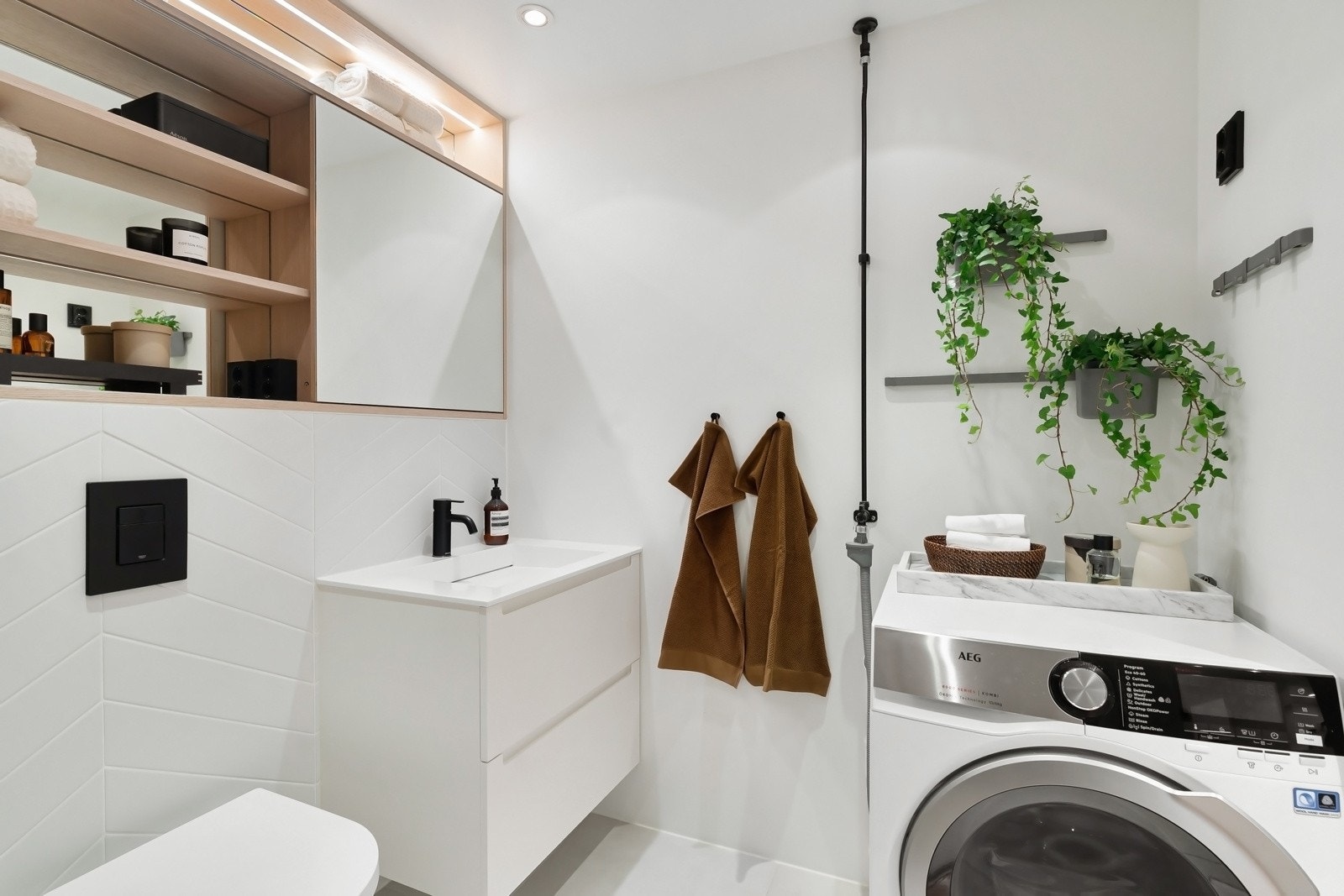 Baderommet har innebygget badekar med dusjdør i glass og regnfallsdusj utført i sort finish. Innebygde hyller i dusjen for oppbevaring. Videre har badet vegghengt toalett og romslig servantskap med heldekkende servant Galleribilde