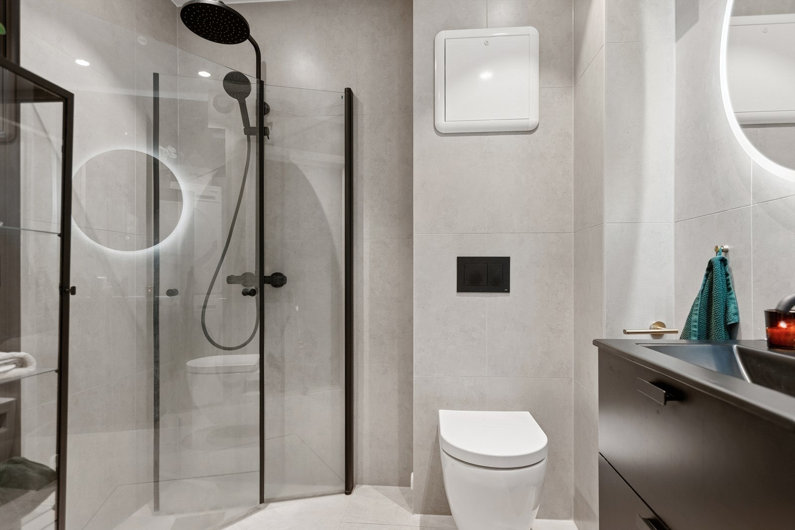 Badet er utstyrt med servantinnredning med skuffer, en overlimt servant, rundt speil med lys, dusjhjørne med innfellbare glassdører og vegghengt toalett. Galleribilde