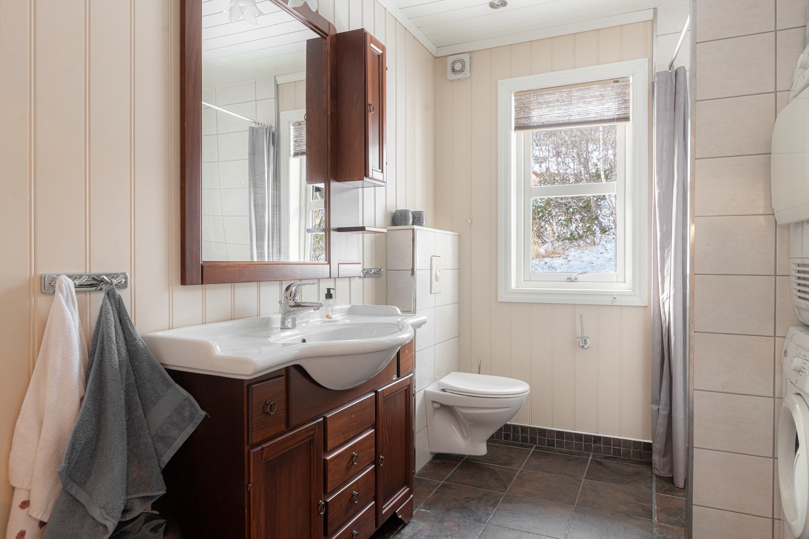 Det andre baderommet har også flis på gulv med varmekabler, flis og malt panel på vegger og hvitmalt panel i himling med integrerte spotter. Her er det pen innredning, lik den som i det andre baderommet, som gir en helhet til våtrommene. Galleribilde