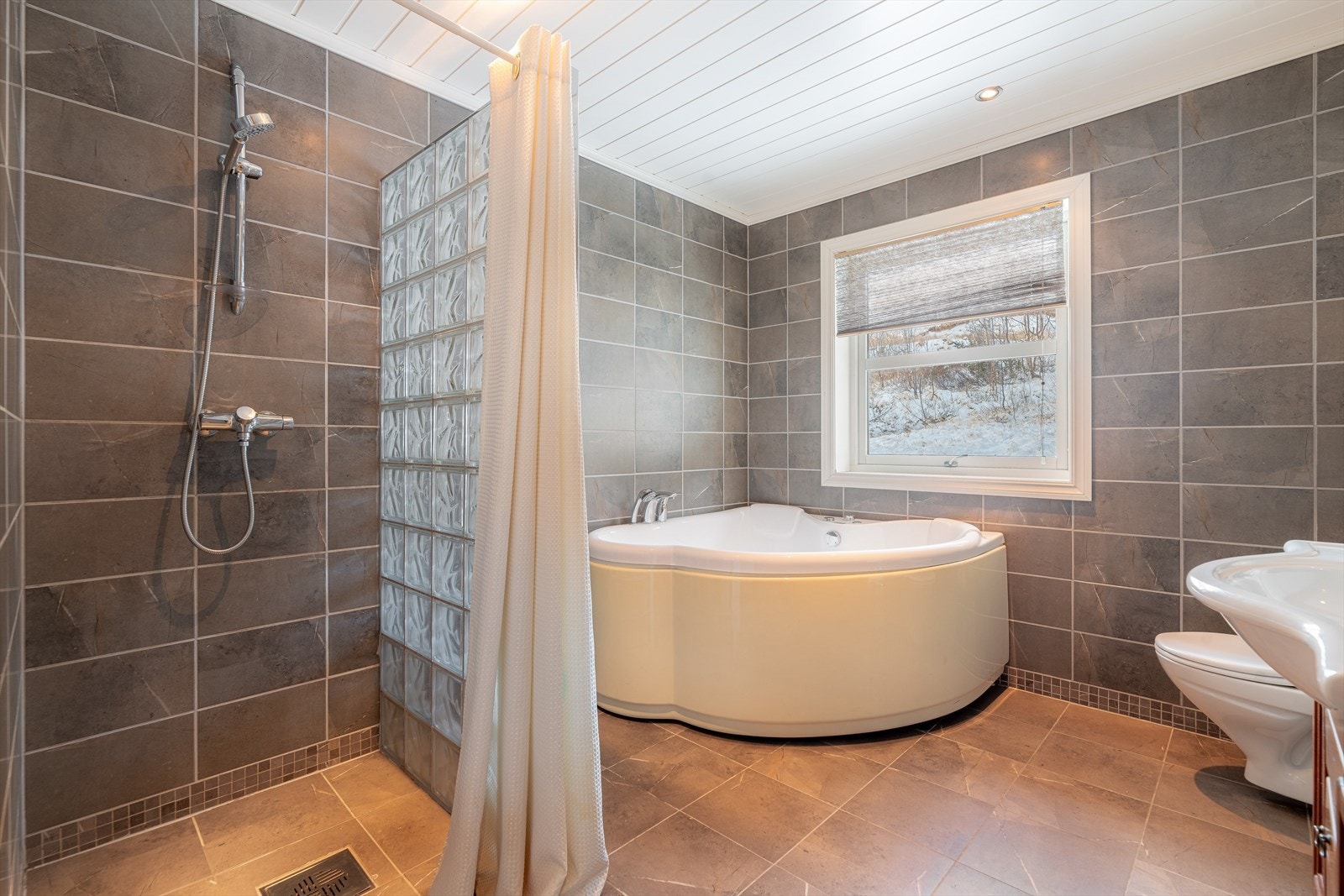 Rommet er utstyrt med pen innredning, veggmontert toalett, hjørnebadekar og dusjnisje. Galleribilde